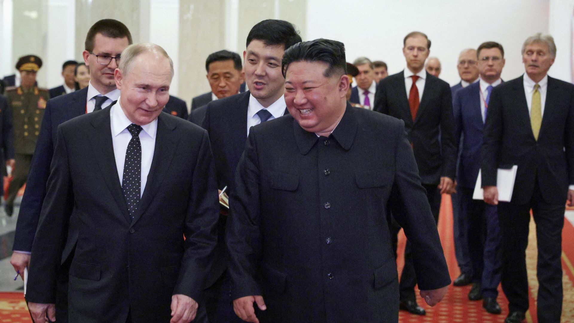 Vladimir Putin, left, walks alongside Kim Jong Un, right, with several men in the background surrounding them. 