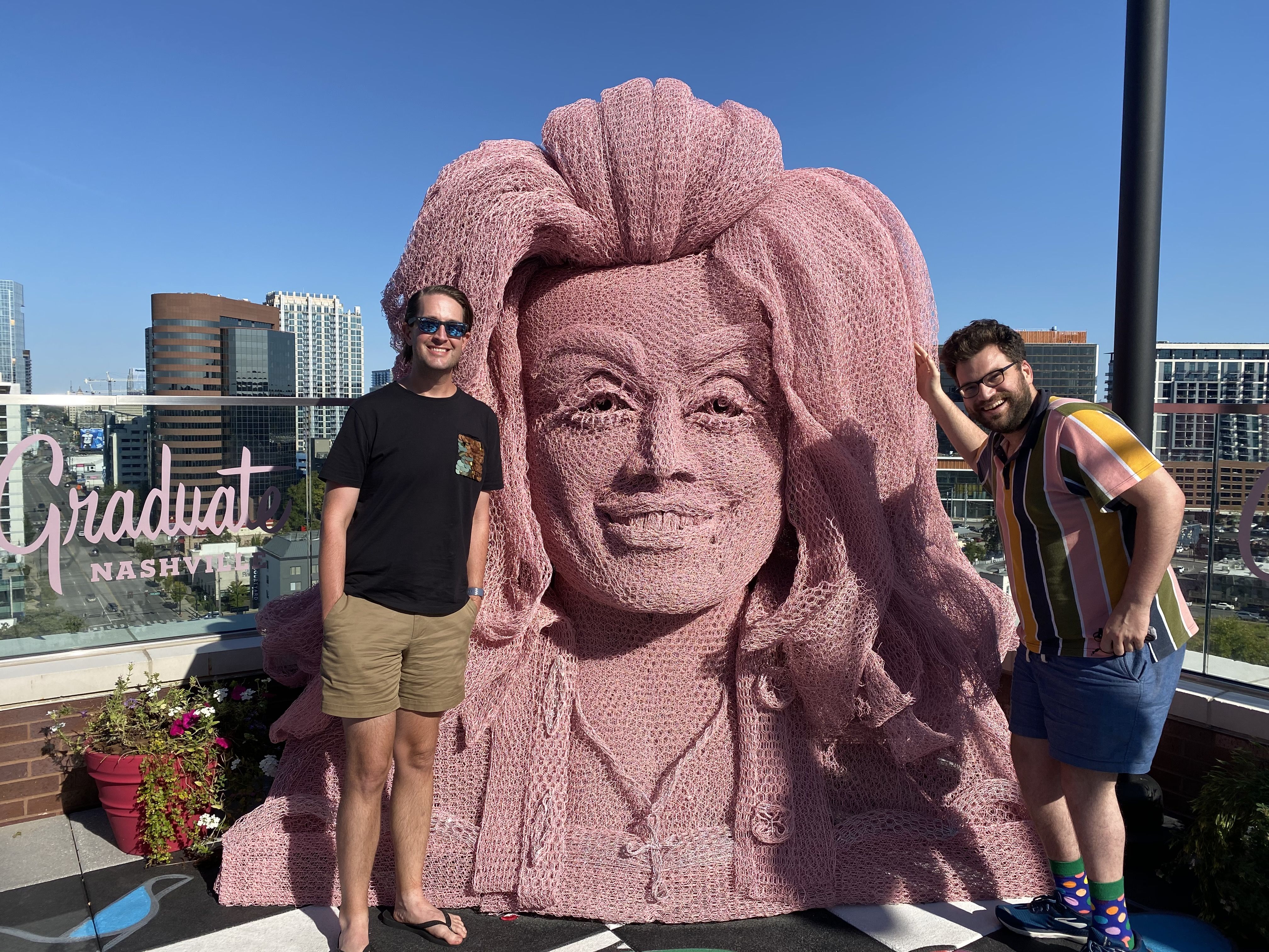 two men pose in front of pink dolly parton statue