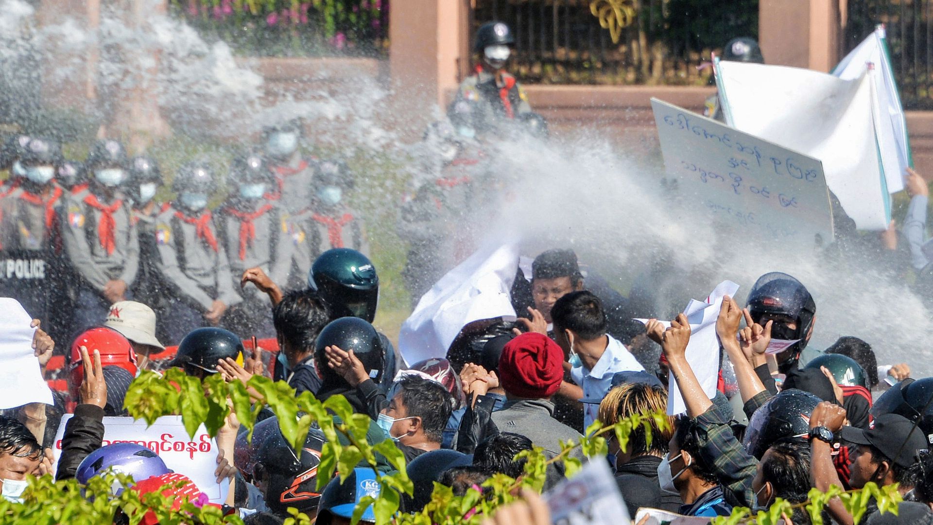 Myanmar police (in background) fire water cannon at protesters as they continue to demonstrate against the February 1 military coup in the capital Naypyidaw on February 9