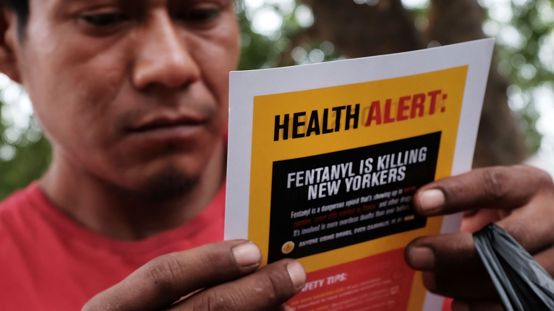 In this image, a man holds up a poster that reads "Health Alert: Fentanyl is killing New Yorkers"