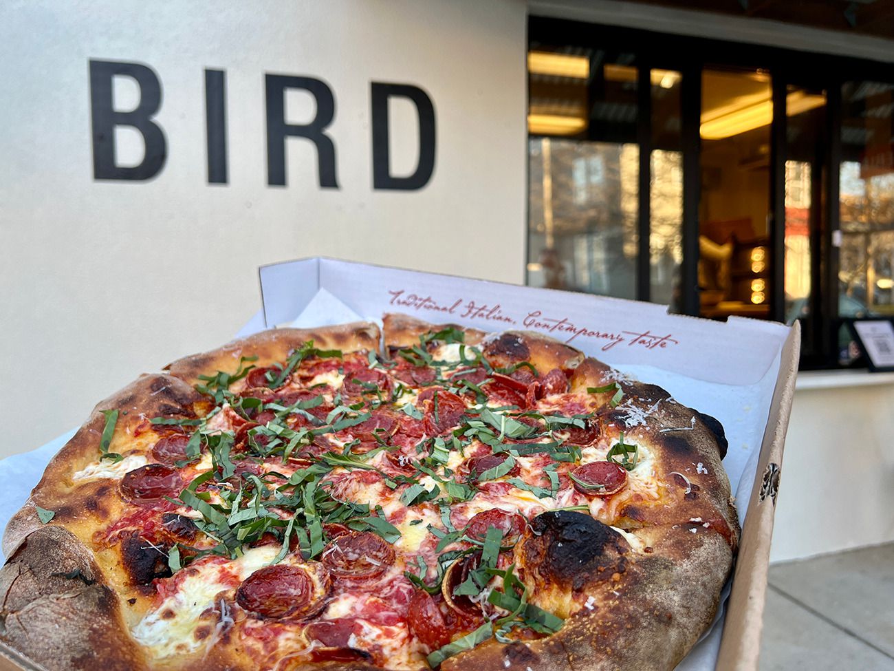 pepperoni pizza in a box in front of a Bird pizza sign