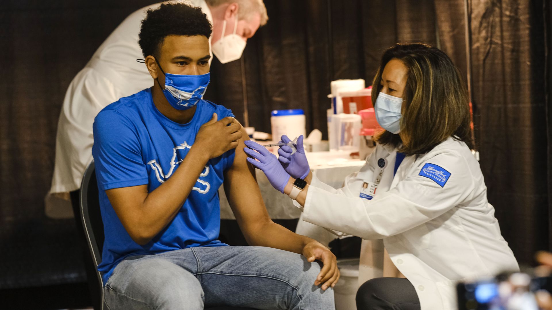 Photo of a masked nurse administering a vaccine to a masked teenager