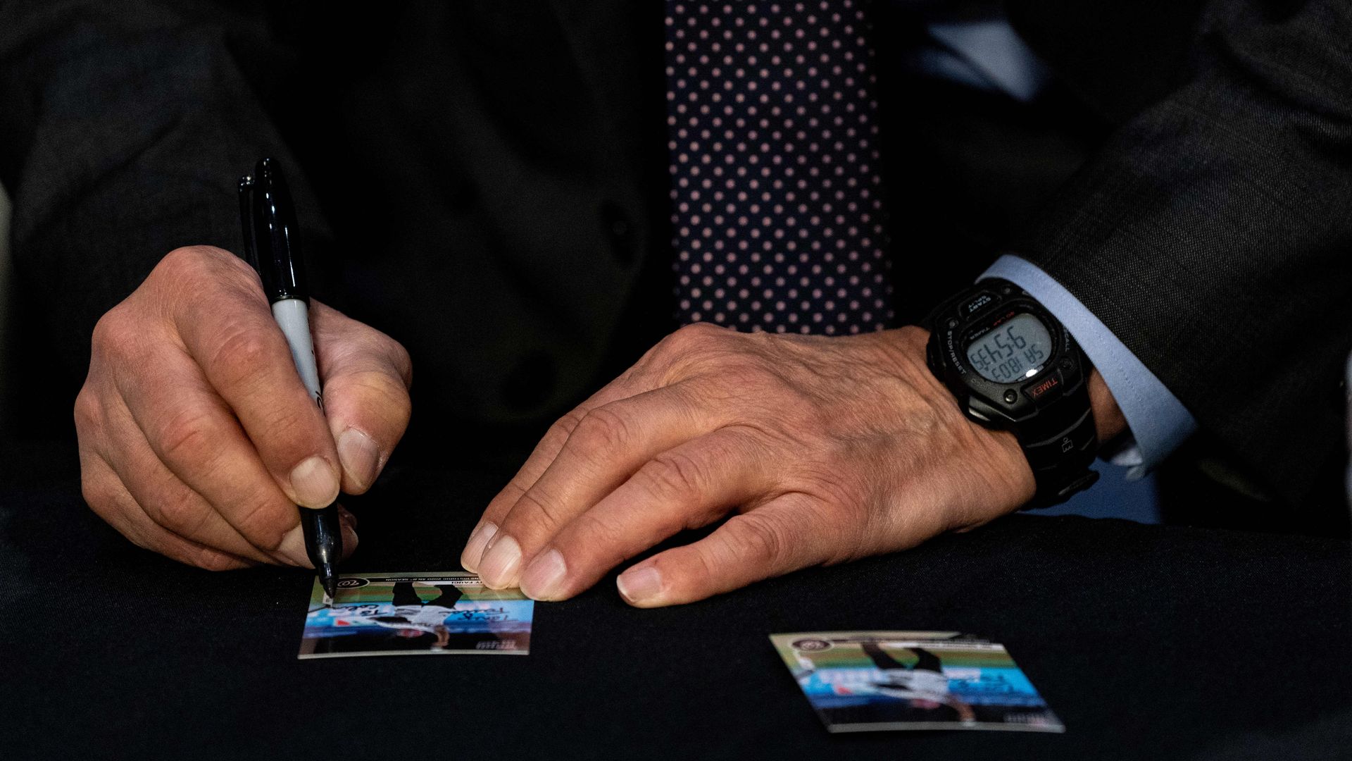 The hands of Anthony Fauci are seen as the doctor signs a baseball card bearing his photo.