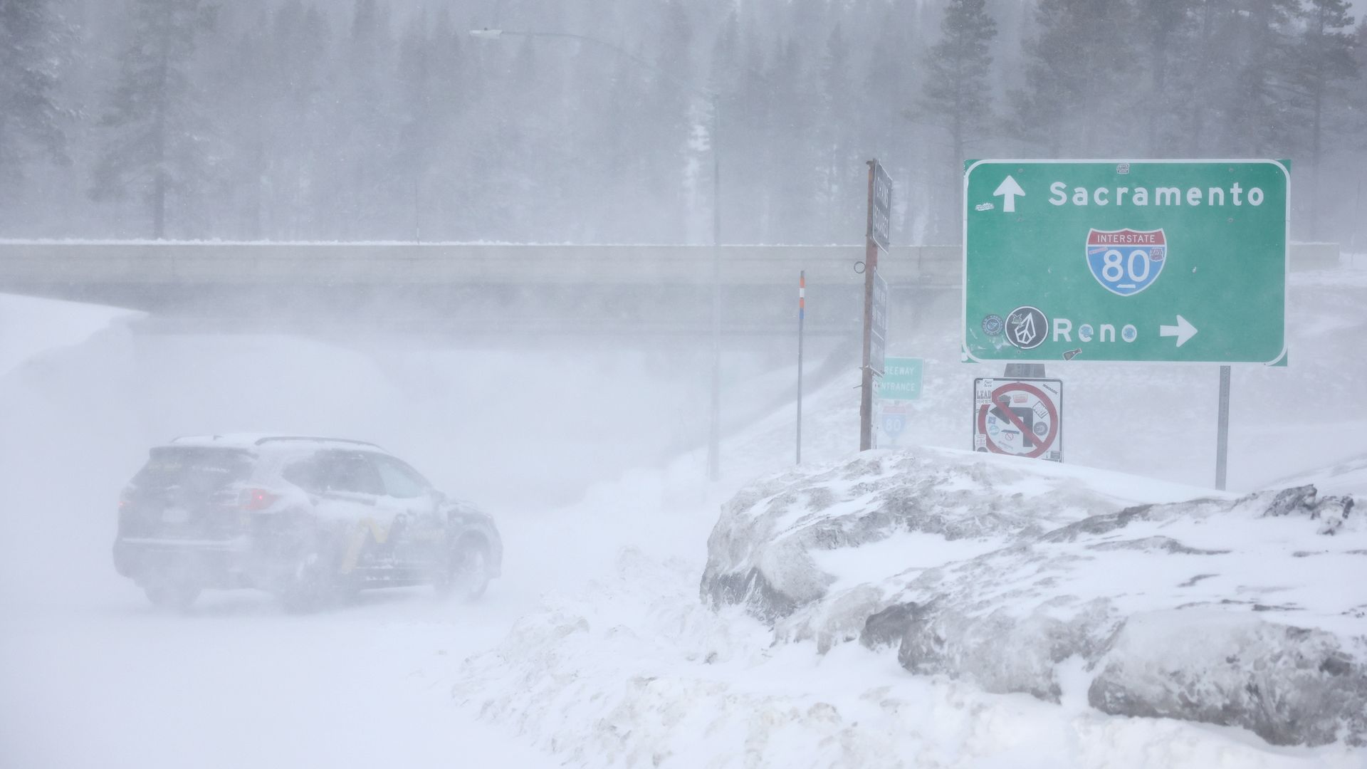 A car drives amid a heavy snowstorm in the higher elevations of California near a road sign saying "Sacramento."