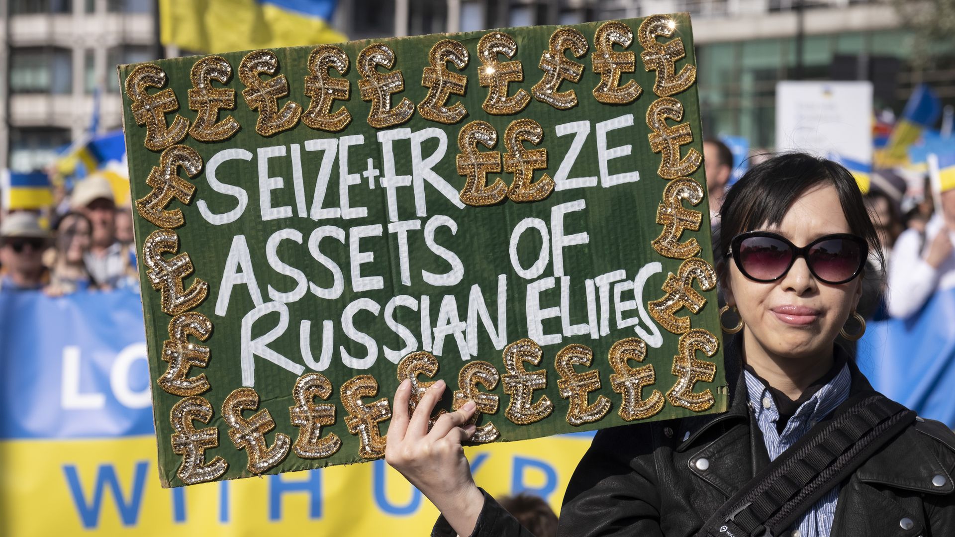 A demonstrator holds a sign demanding the seizure of Russian elites' assets.