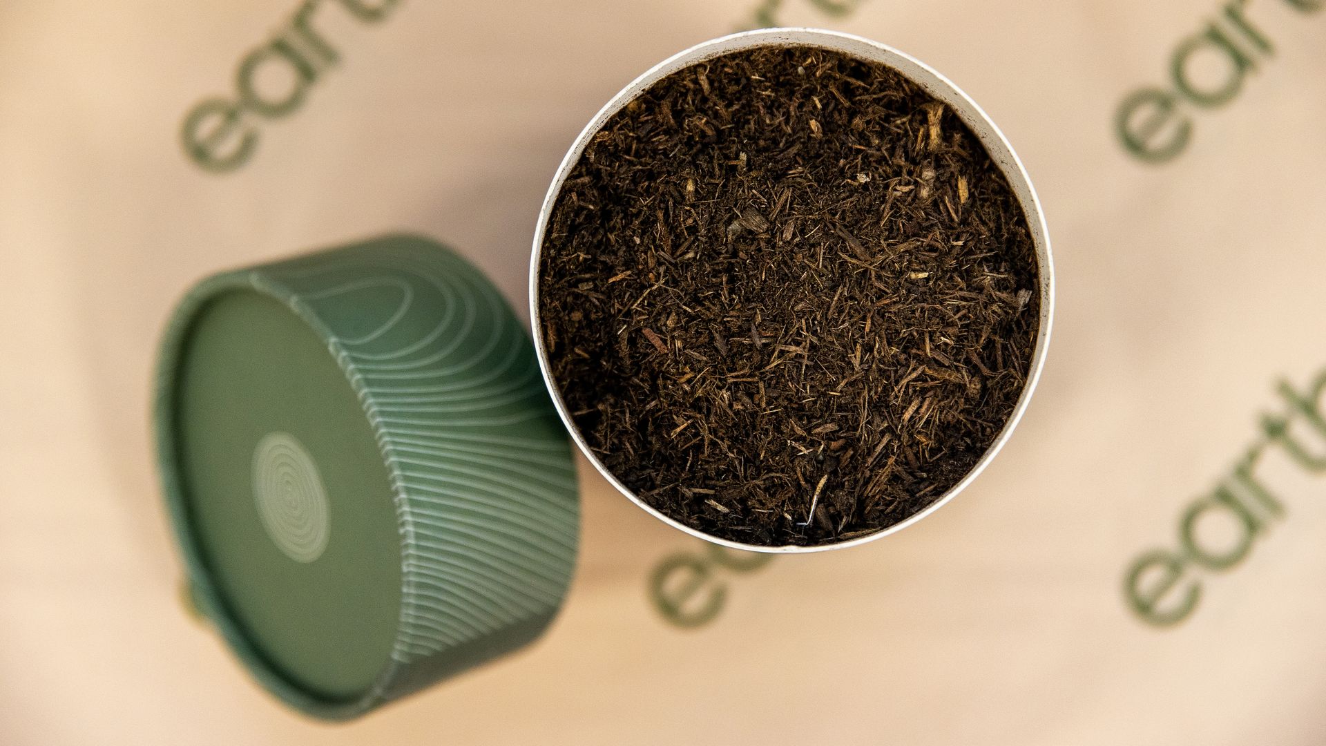 A 2023 photo shows an aerial view of a container filled with human compost, with the container's cap next to it in Earth Funeral's office in Auburn, Washington. It's sitting on a table with paper that says "earth" in multiple places.