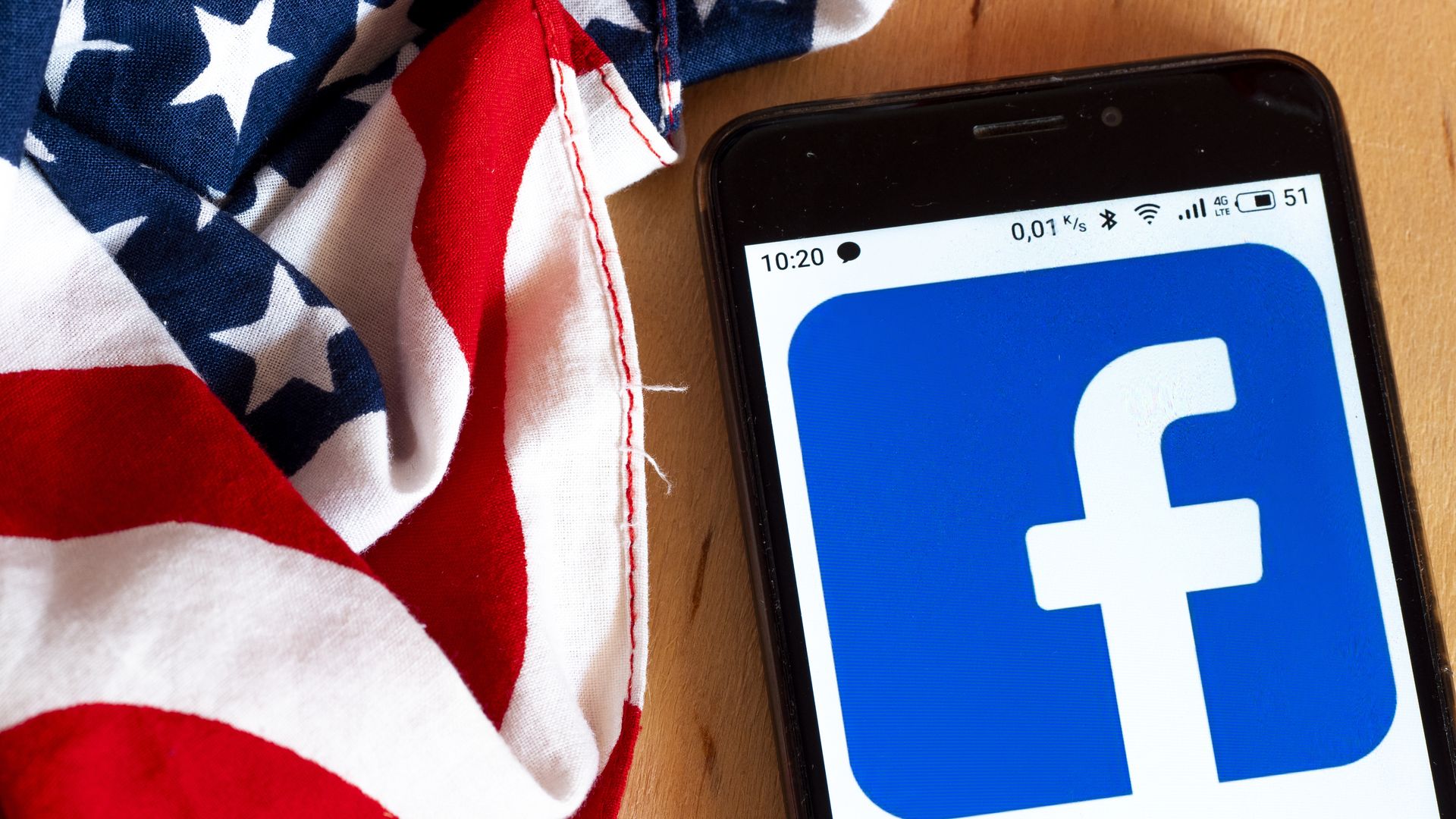 A photo of a smartphone displaying the Facebook logo with an American flag draped near it