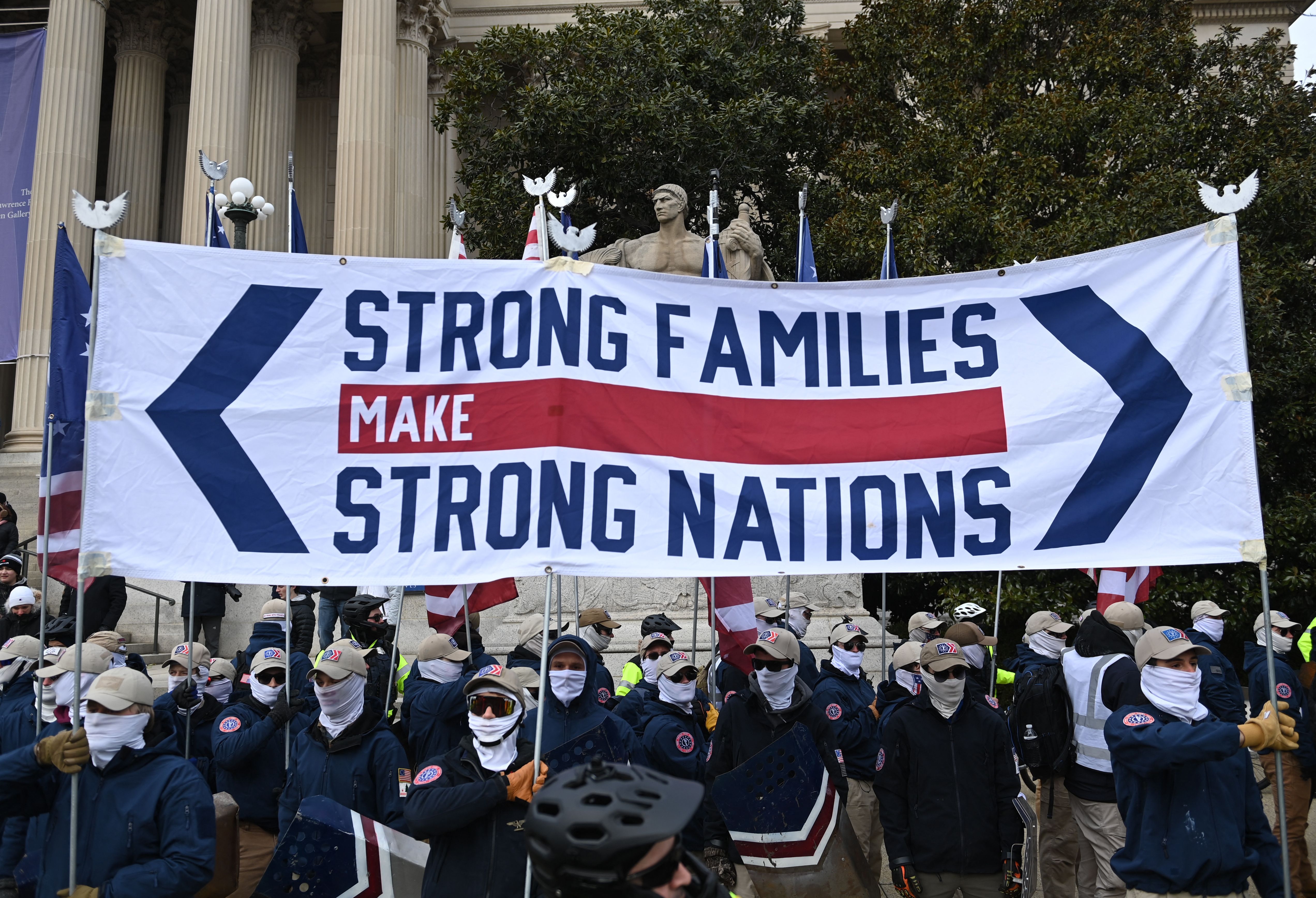 Photo of a group of people wearing masks and holding a banner that says "Strong families make strong nations"