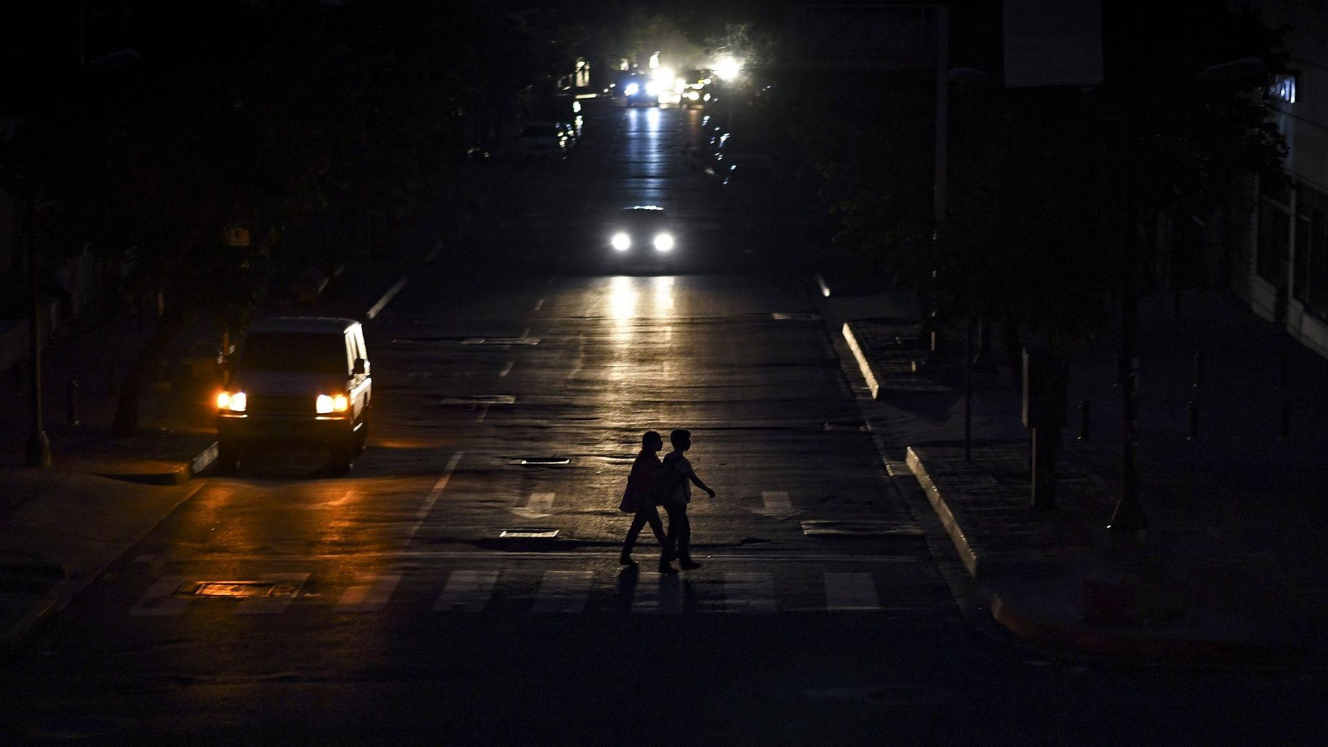 People are silhouetted by the lights of a vehicle as they cross a street in Caracas on July 22.