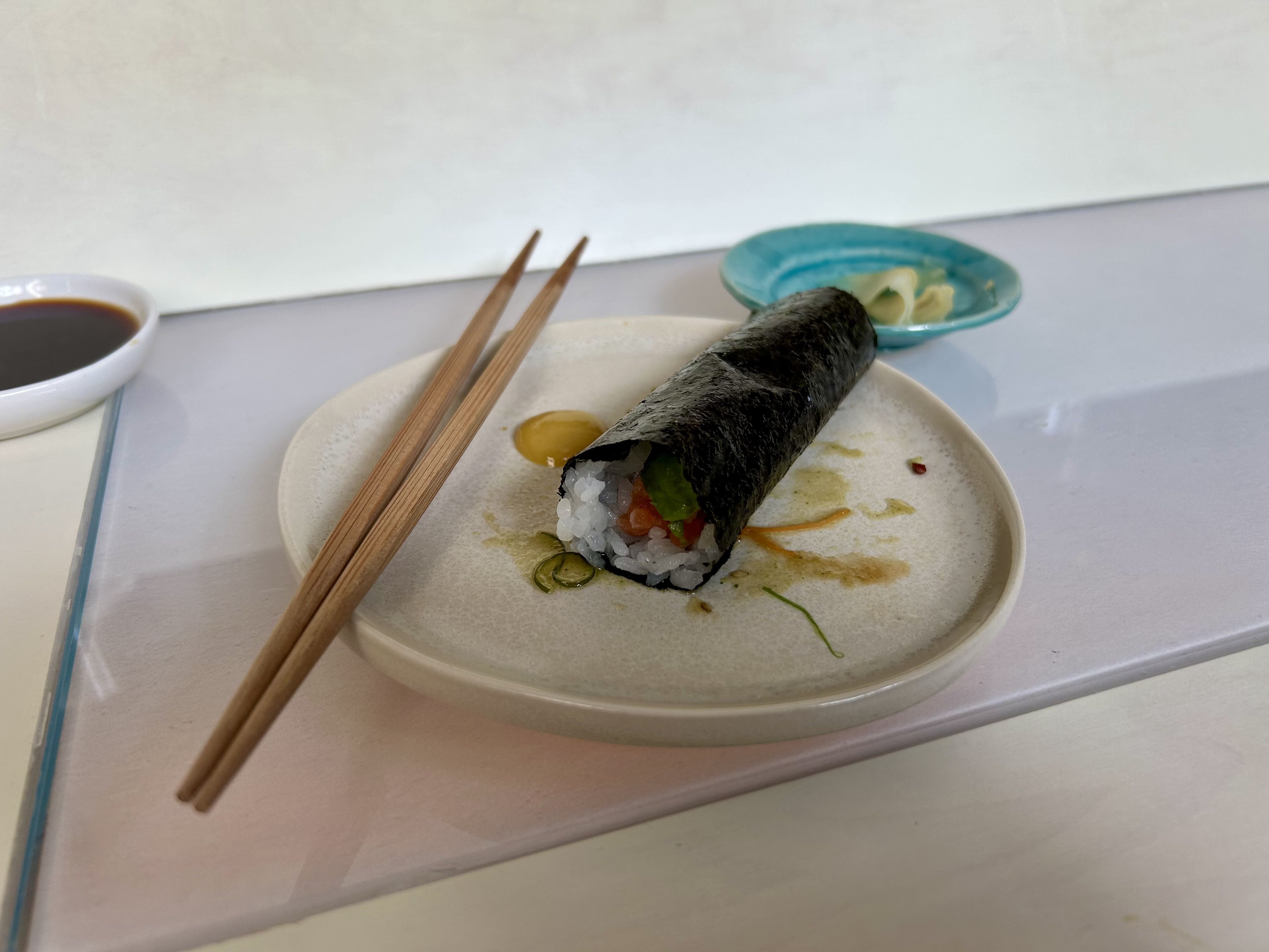 A hand roll with chopsticks on a plate. 
