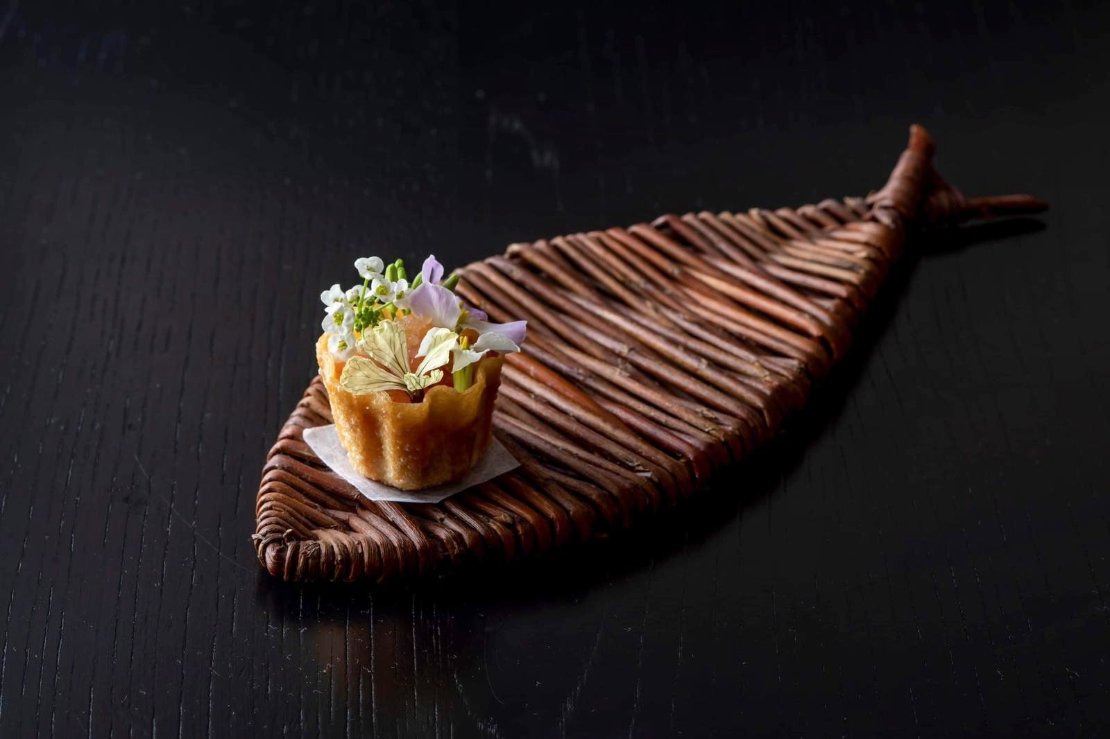 A woven plate of sticks shaped like a fish bolsters a pastry filled with flowers