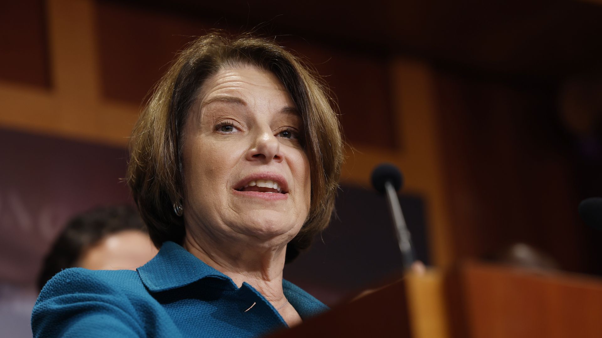 Amy Klobuchar standing at a podium with a blue jacket