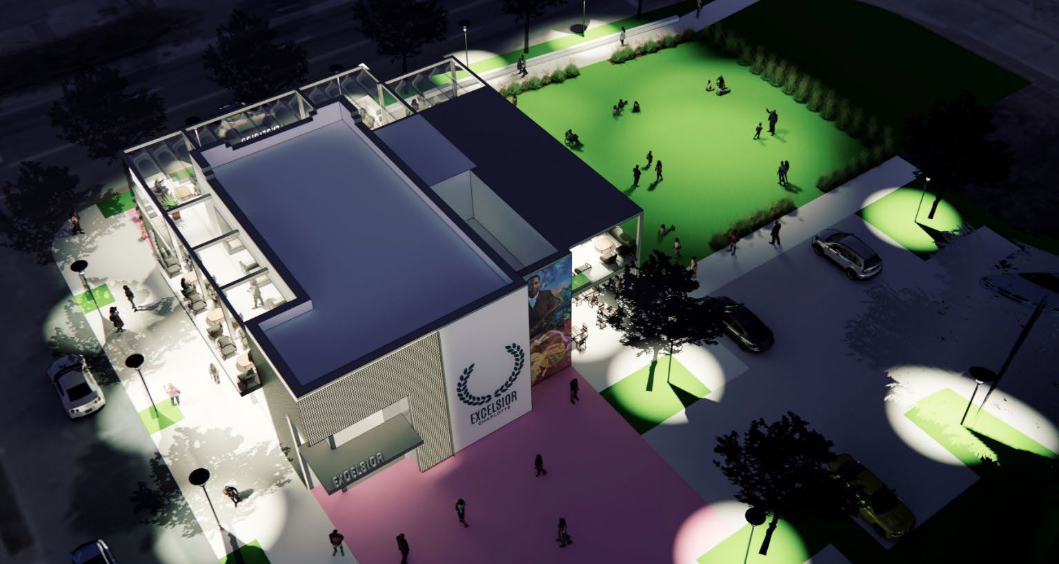 A nighttime aerial view of the Excelsior Complex with lit walkways and green lawn area where people gather, illuminated by streetlights and surrounded by parked cars and trees.