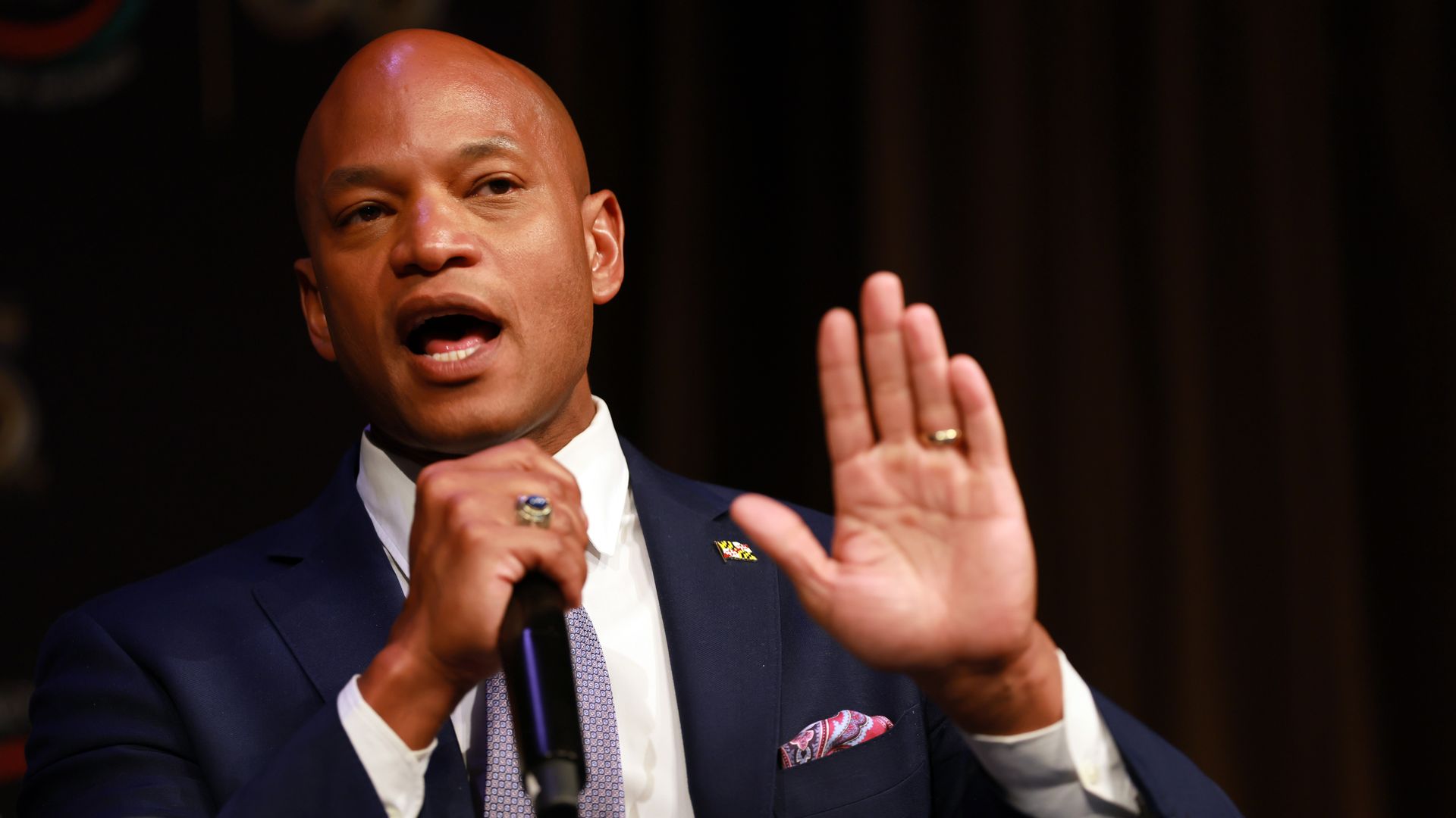 Wes Moore speaks into a microphone while raising his left hand.