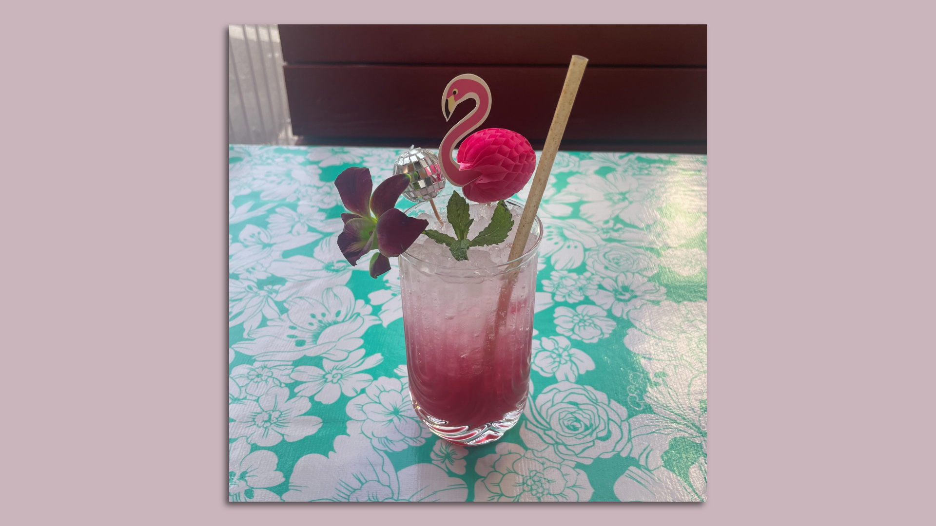 A photo of a pink drink on a table with a miniature flamingo and disco ball.