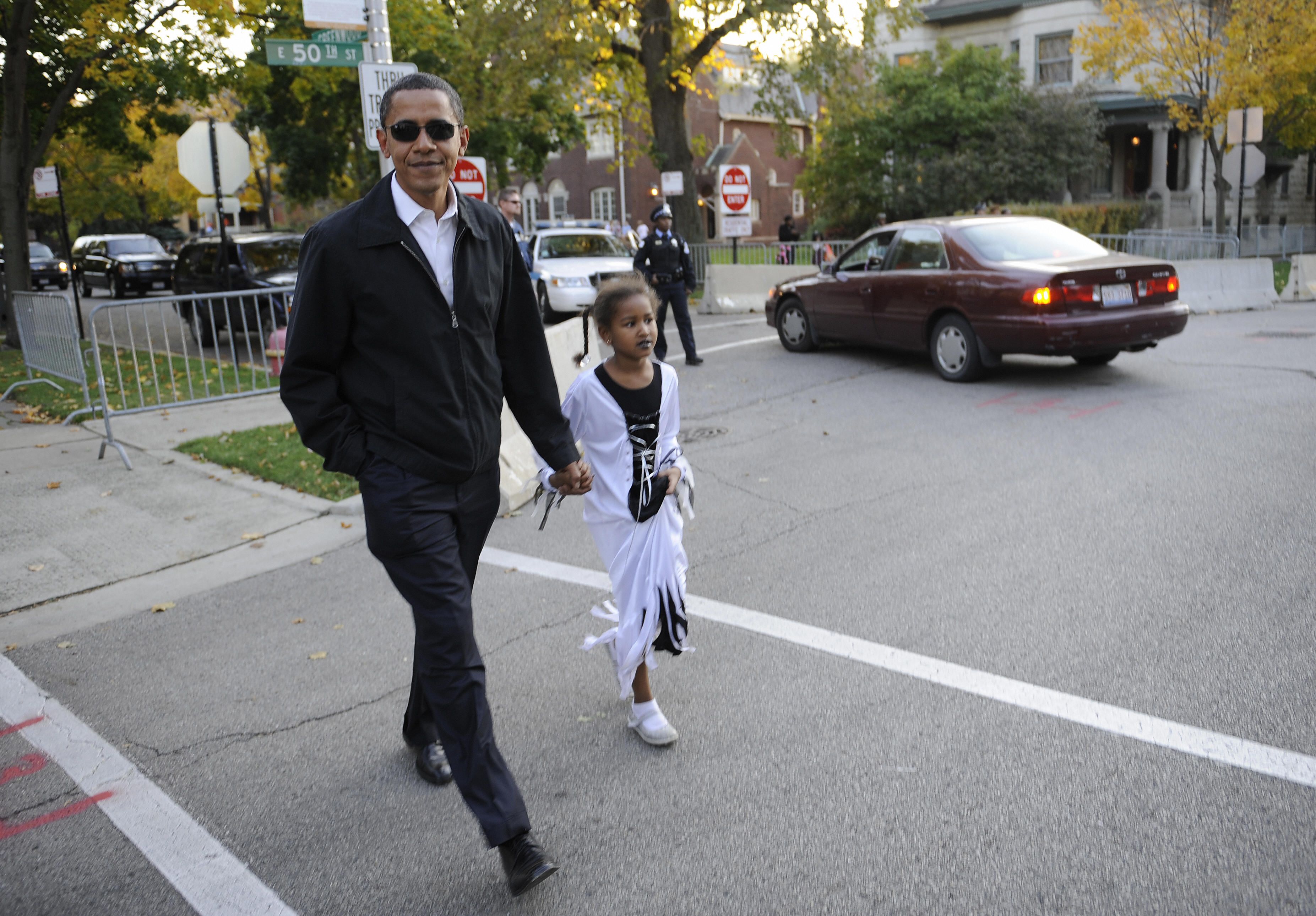 Photo of a man holding hands with his daughter while they trick-or-treat.
