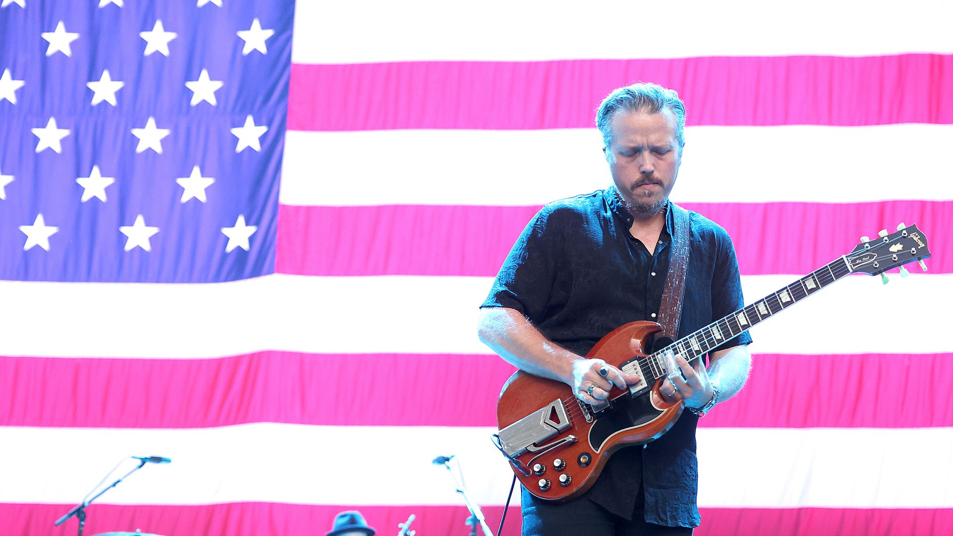 Musician Jason Isbell plays a guitar in front of a giant American flag