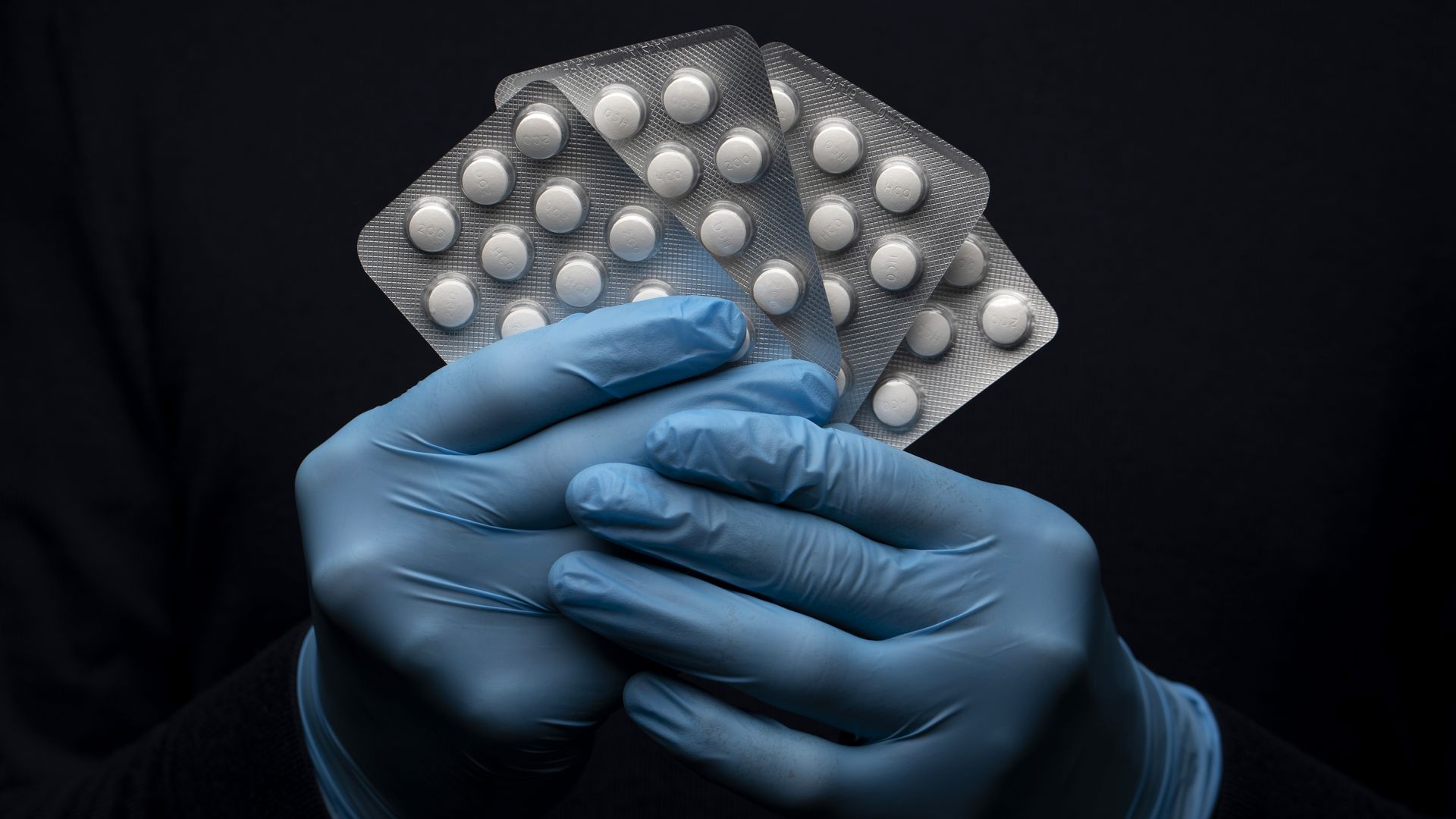 Gloved hands holding packets of hydroxychloroquine tablets