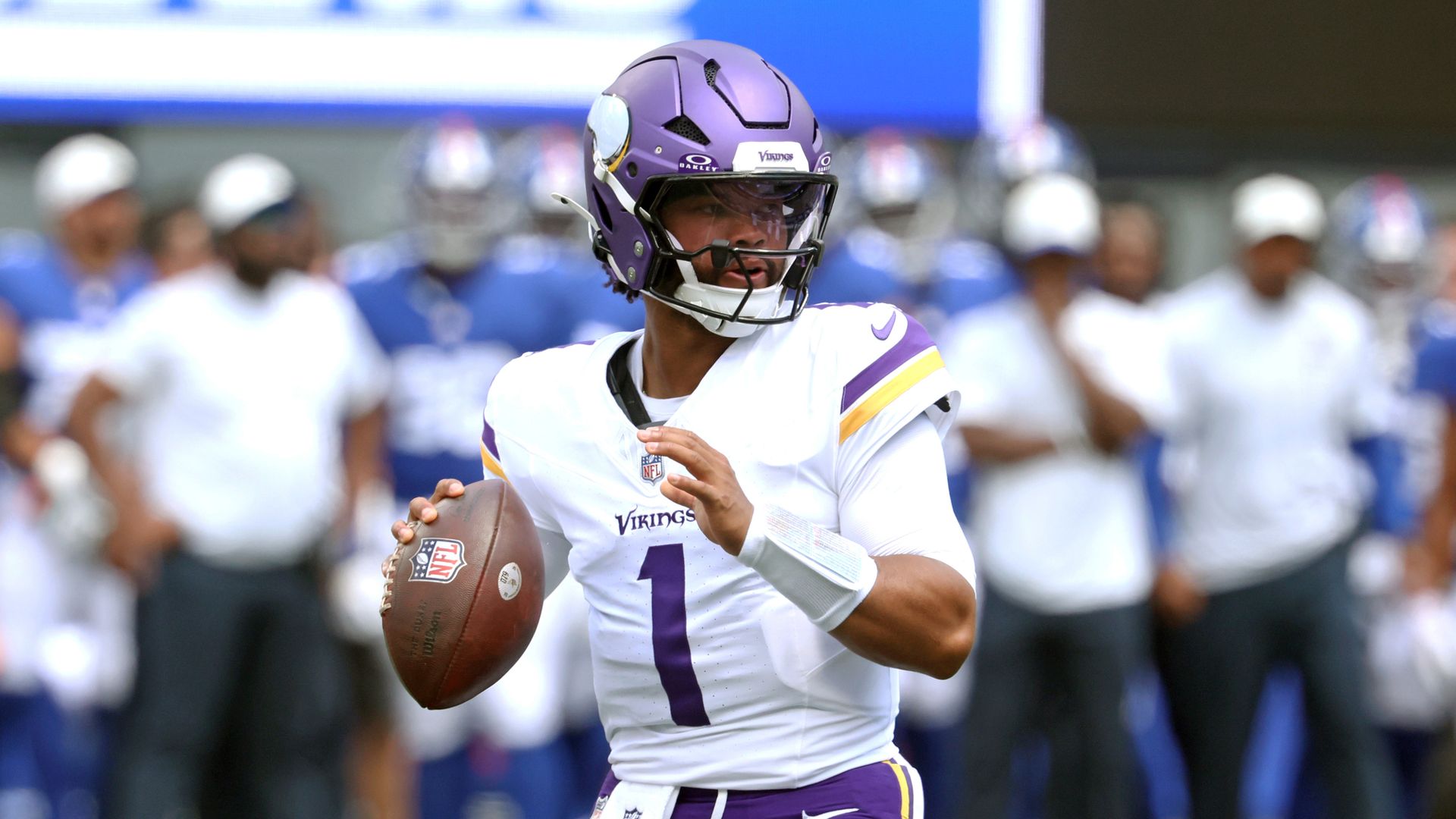 Kyler Murray r in a white jersey with purple and gold trim, wearing a purple helmet, holding a football as fans blur in the background.