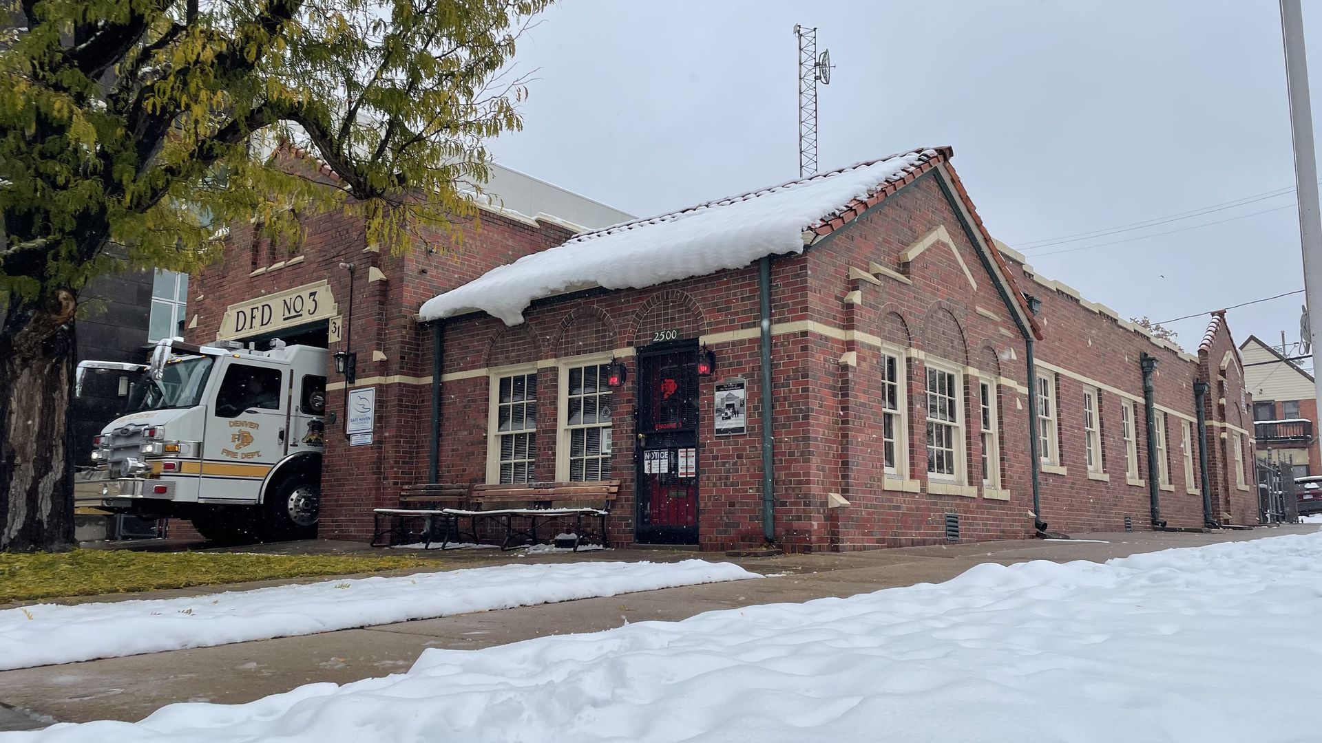 A white fire truck pulls into a small, brick firehouse.