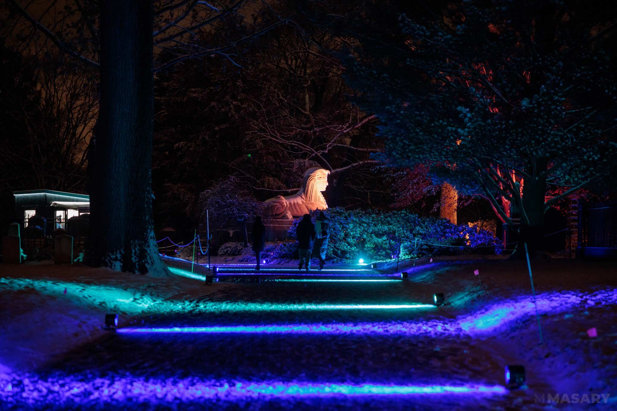 Blue and teal lights flow through Mount Auburn Cemetery near the Sphynx statue.