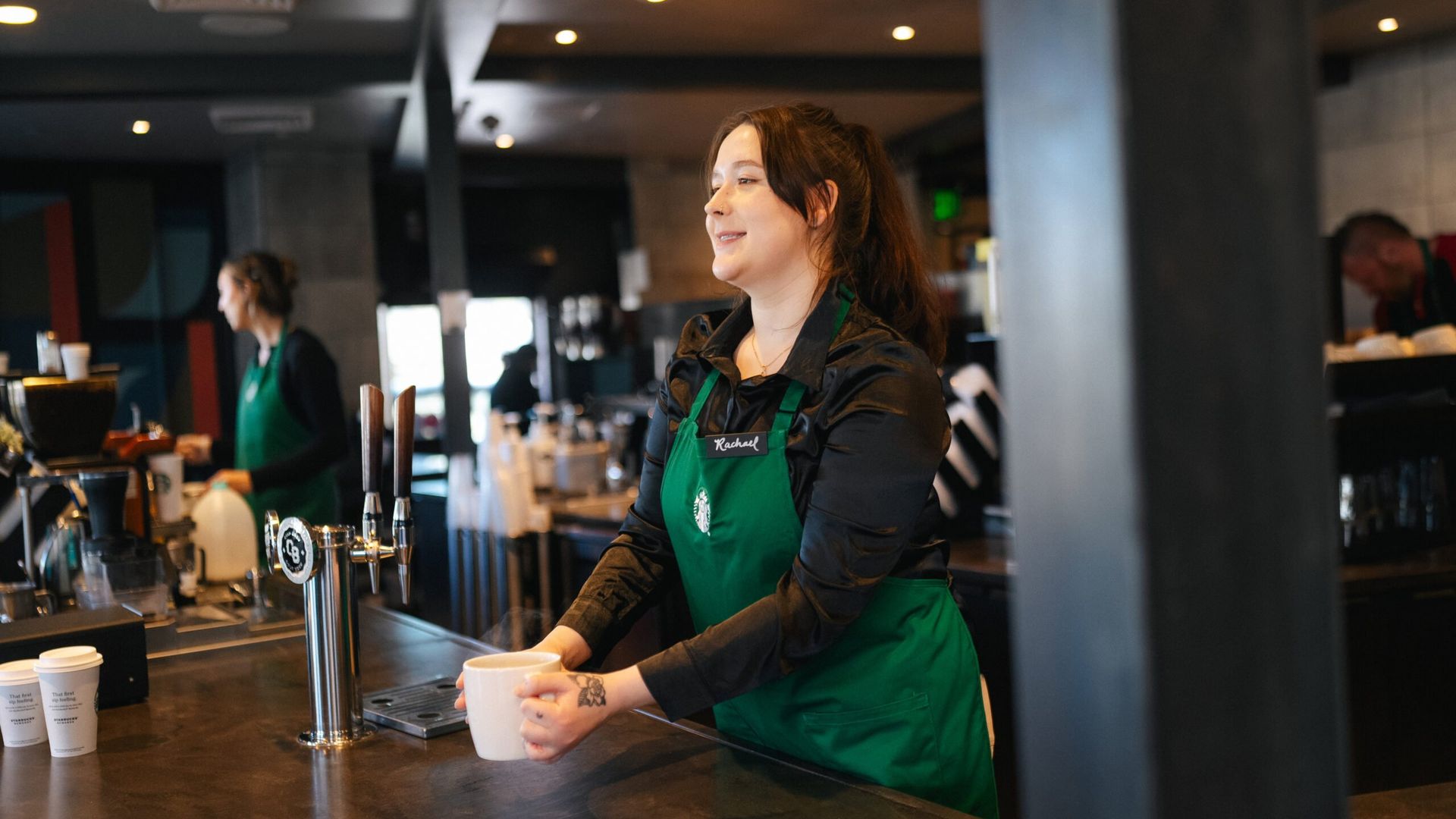 Starbucks baristas wearing black shirts with green aprons making coffee drinks