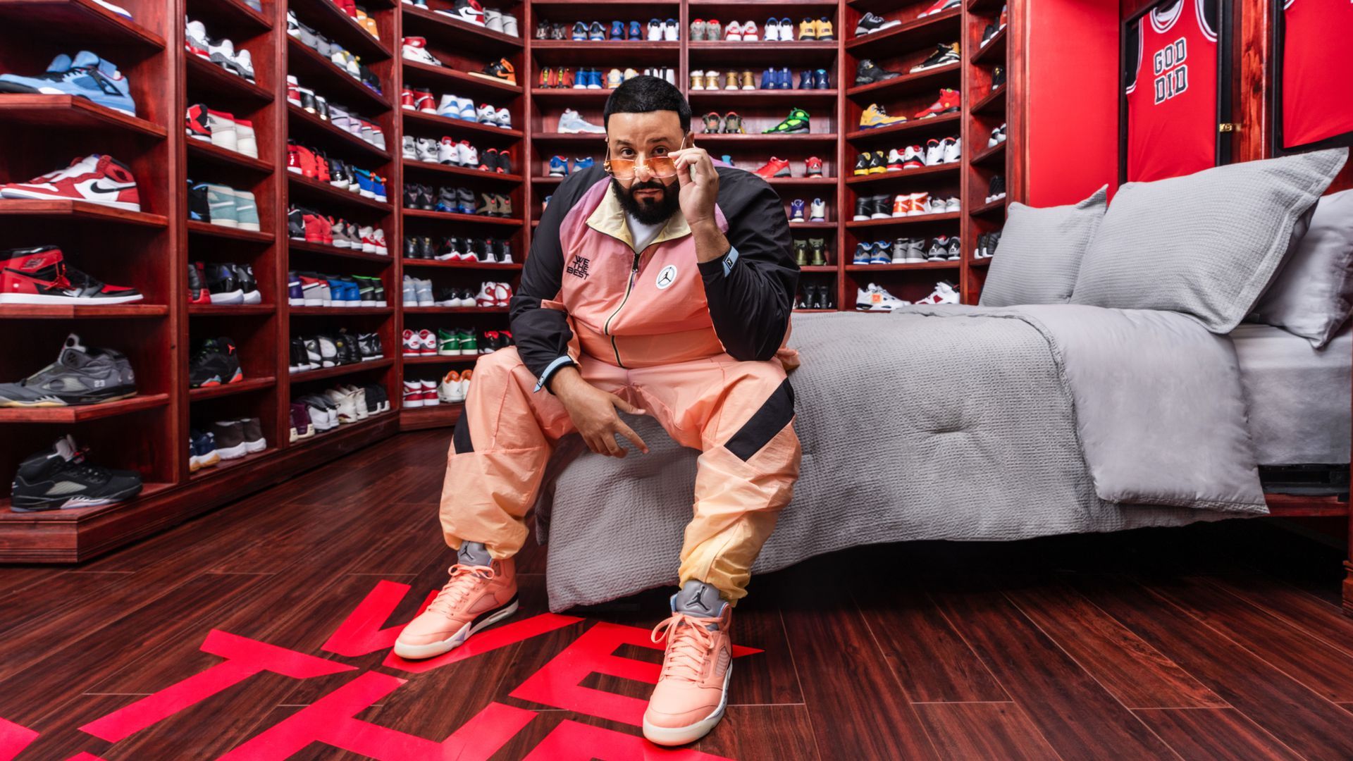 DJ Khaled seated in room filled with shelves of shoes.