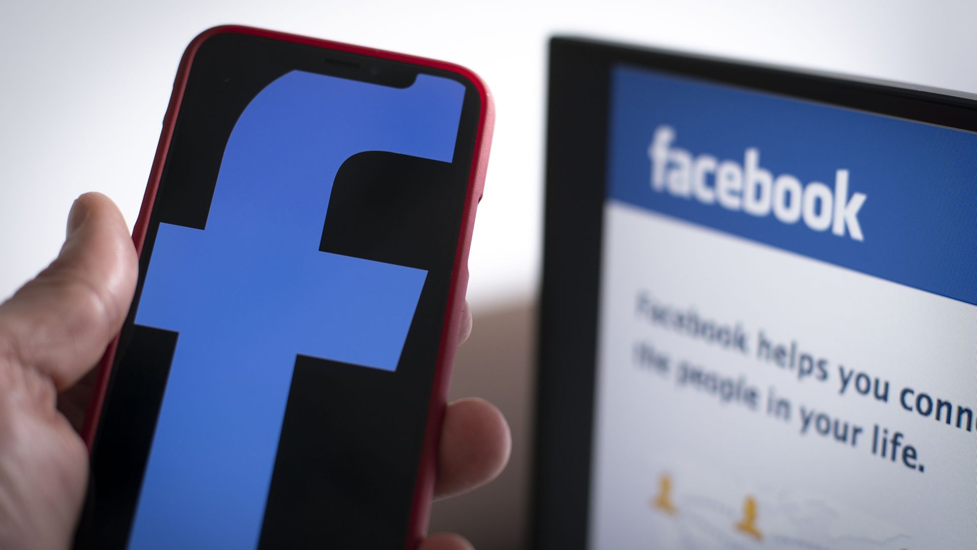 The Facebook logo is seen on a mobile device with the Facebook login screen in the background.