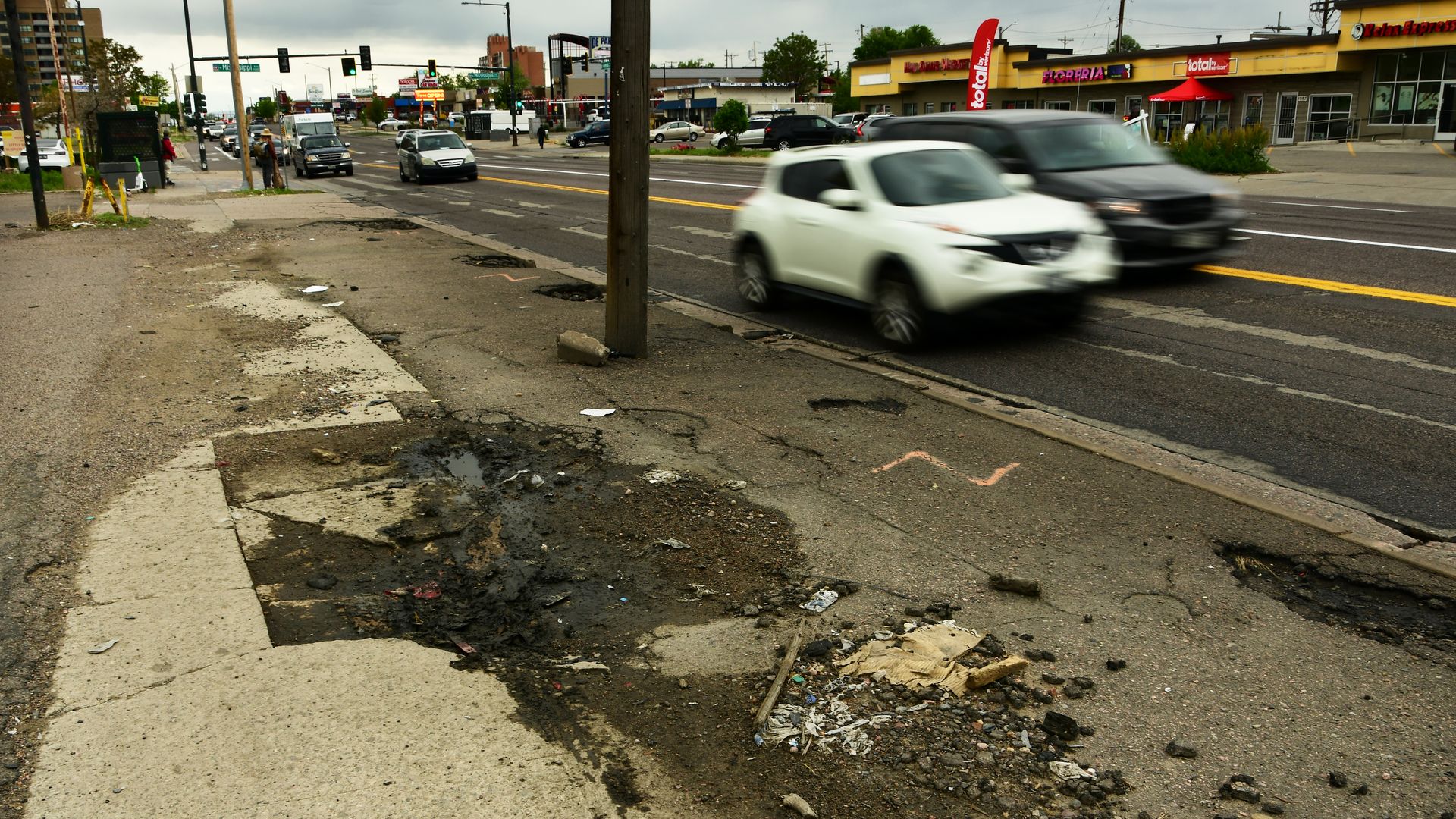 Heavily damaged and unkept sidewalk near cars along a road. 