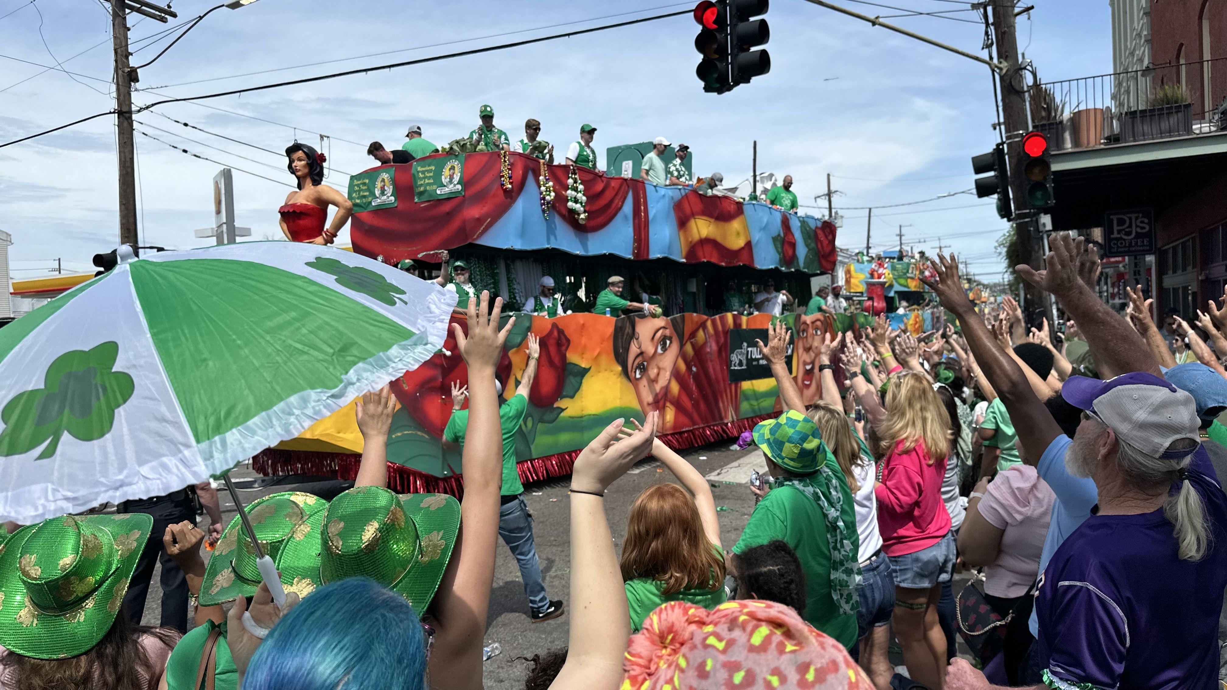 A green and shamrock-covered parasol is held up as a parade float passes by a crowd.