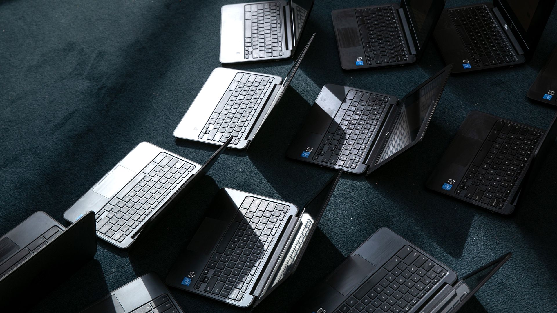 Multiple laptops arranged in rows on a dark blue carpet, open and angled, silver and black bodies with blue stickers.