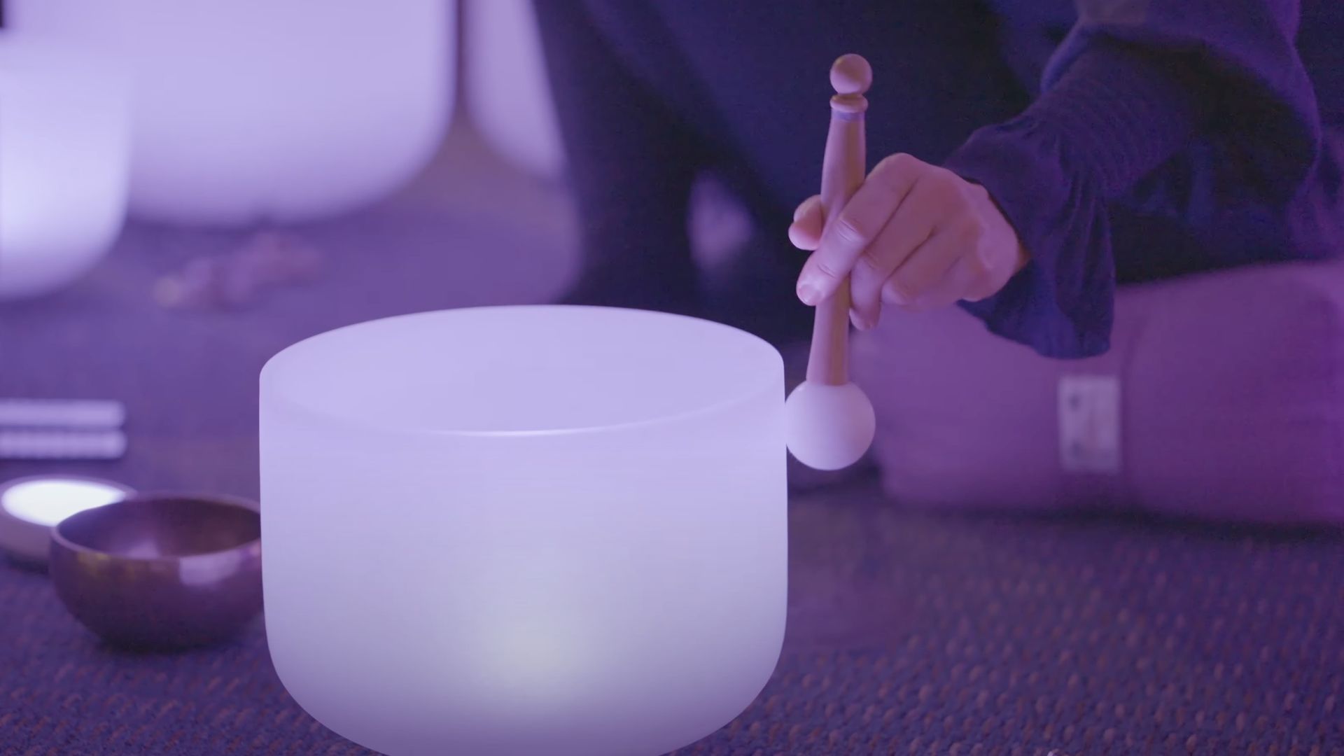 A woman plays a quartz crystal bowl with a rubber mallet in a sound bath