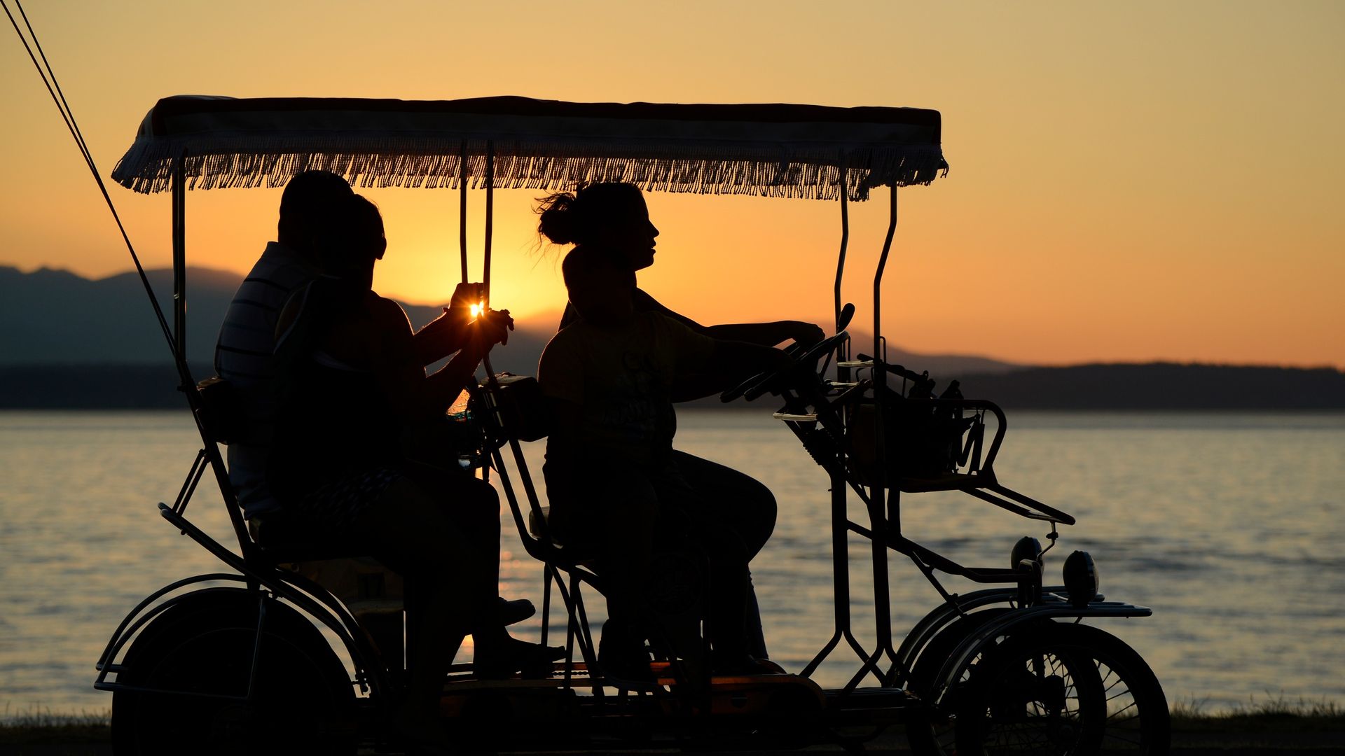 People ride in a surrey cart along Alki Beach in Seattle at sunset. 