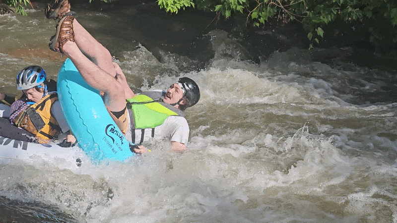 A tuber watches as another tuber flips in a rapid.