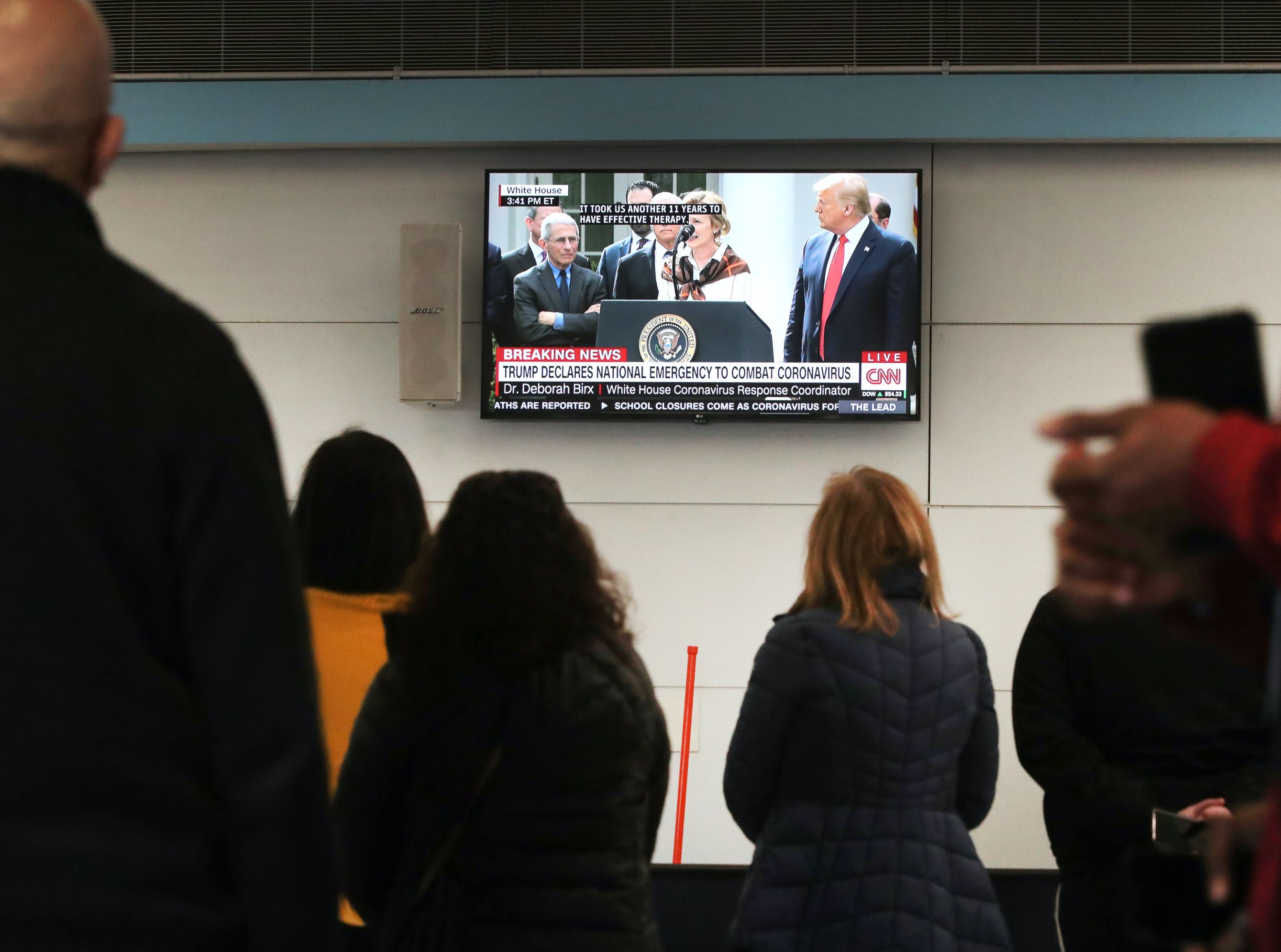  People waiting to meet travelers arriving at O'Hare Airport watch as U.S. President Trump hold a news conference about the coronavirus pandemic on March 13, 2020 in Chicago, Illinois. 