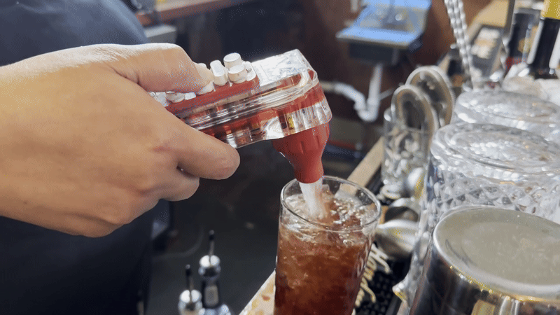 A person's hand pushes a soda gun to pour root beer into a glass.
