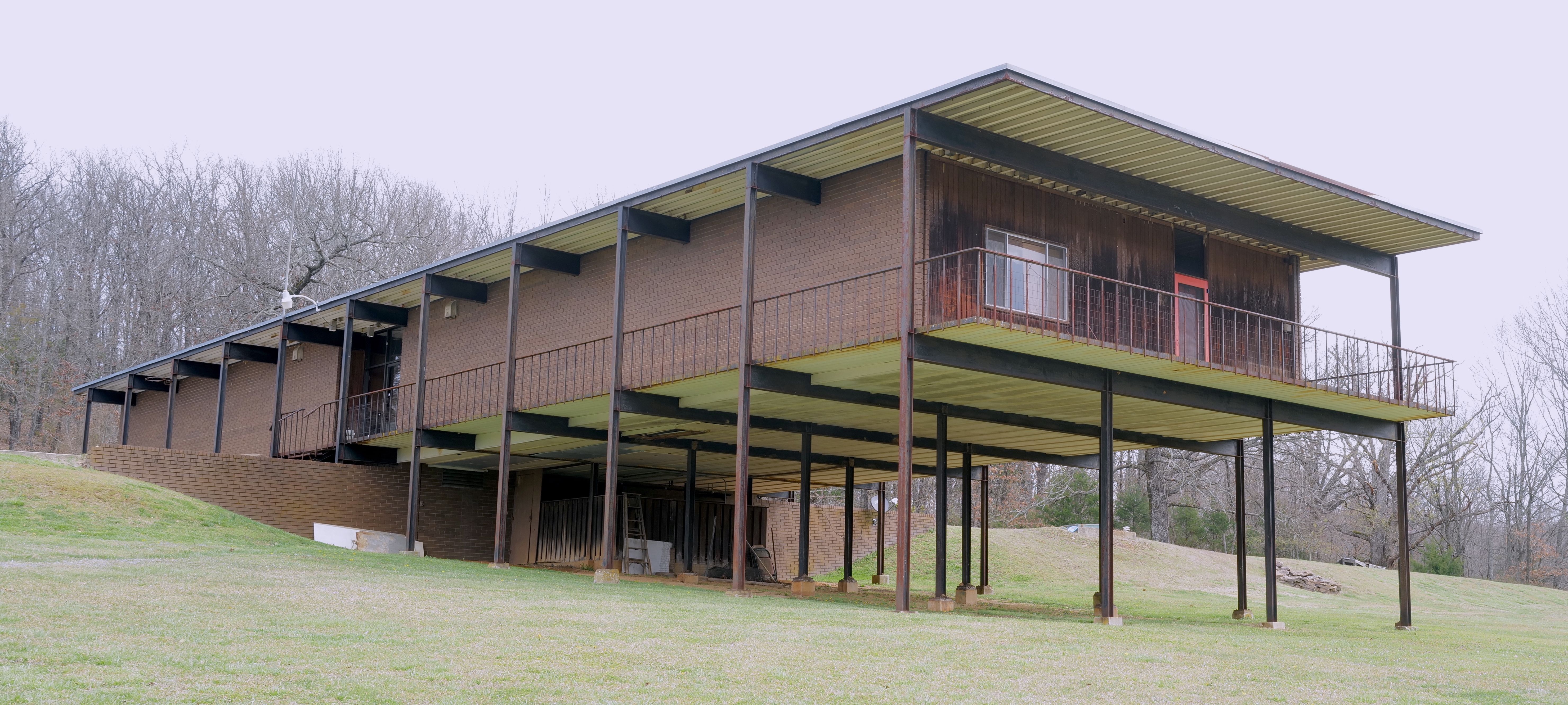 A photo of a long brick building cantilevered over a green lawn.