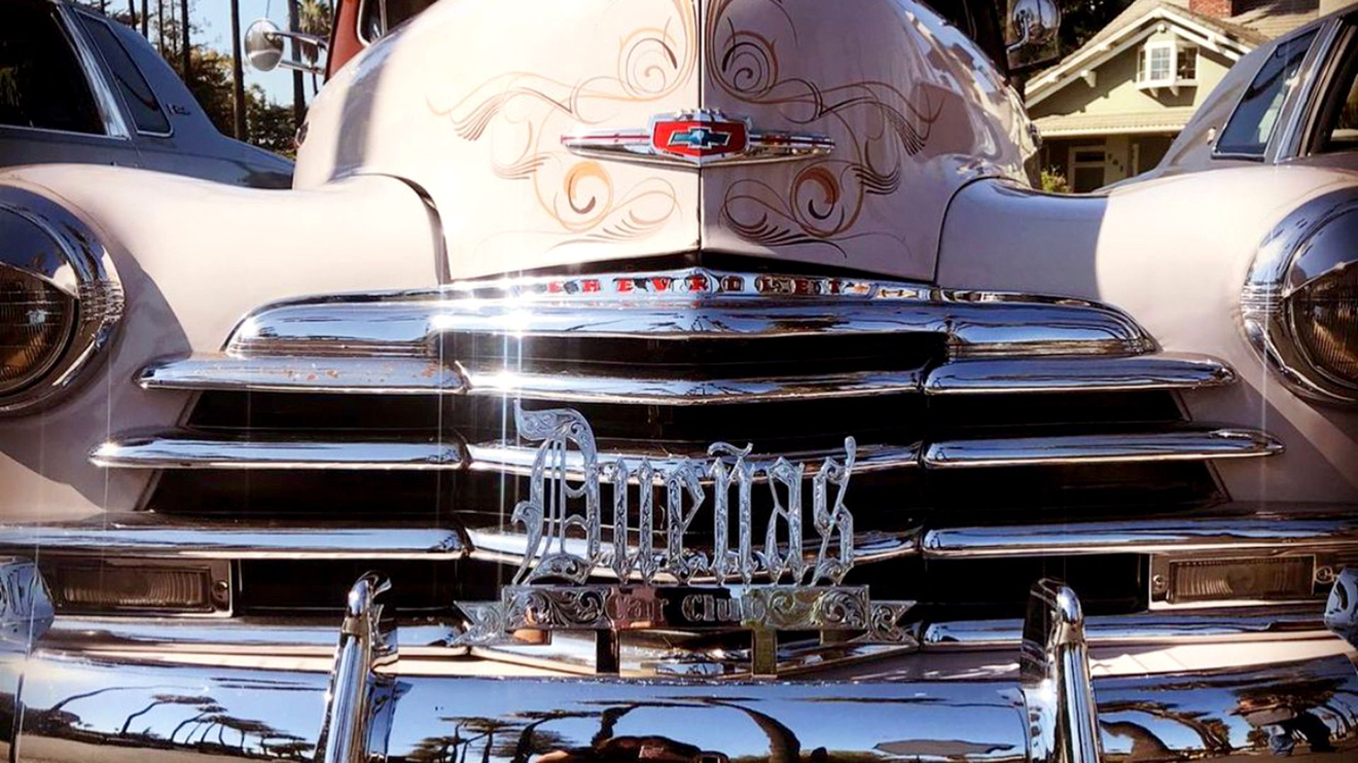 a powder pink vintage lowrider with the spanish word for "women owners" in chrome on the front grill