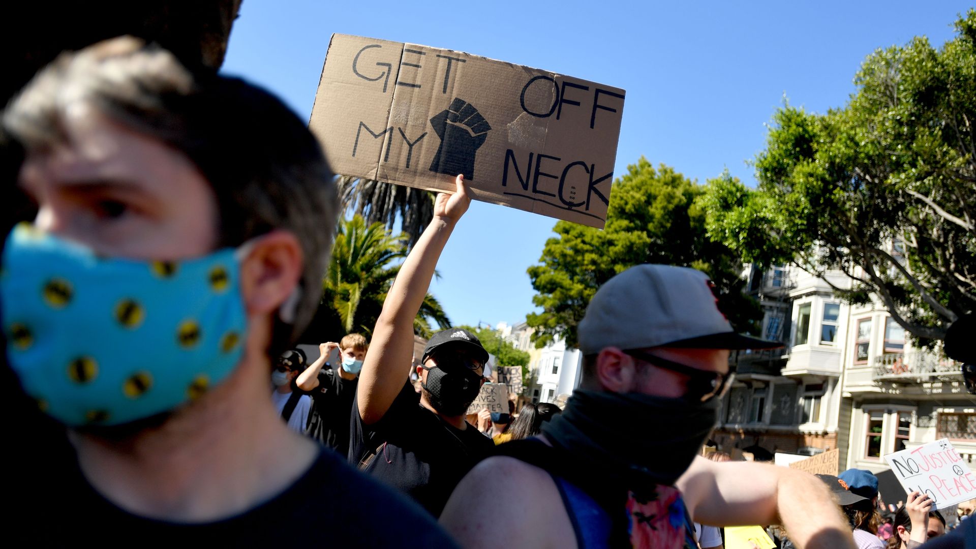 Photo of a masked protester holding a sign that says "Get off my neck"