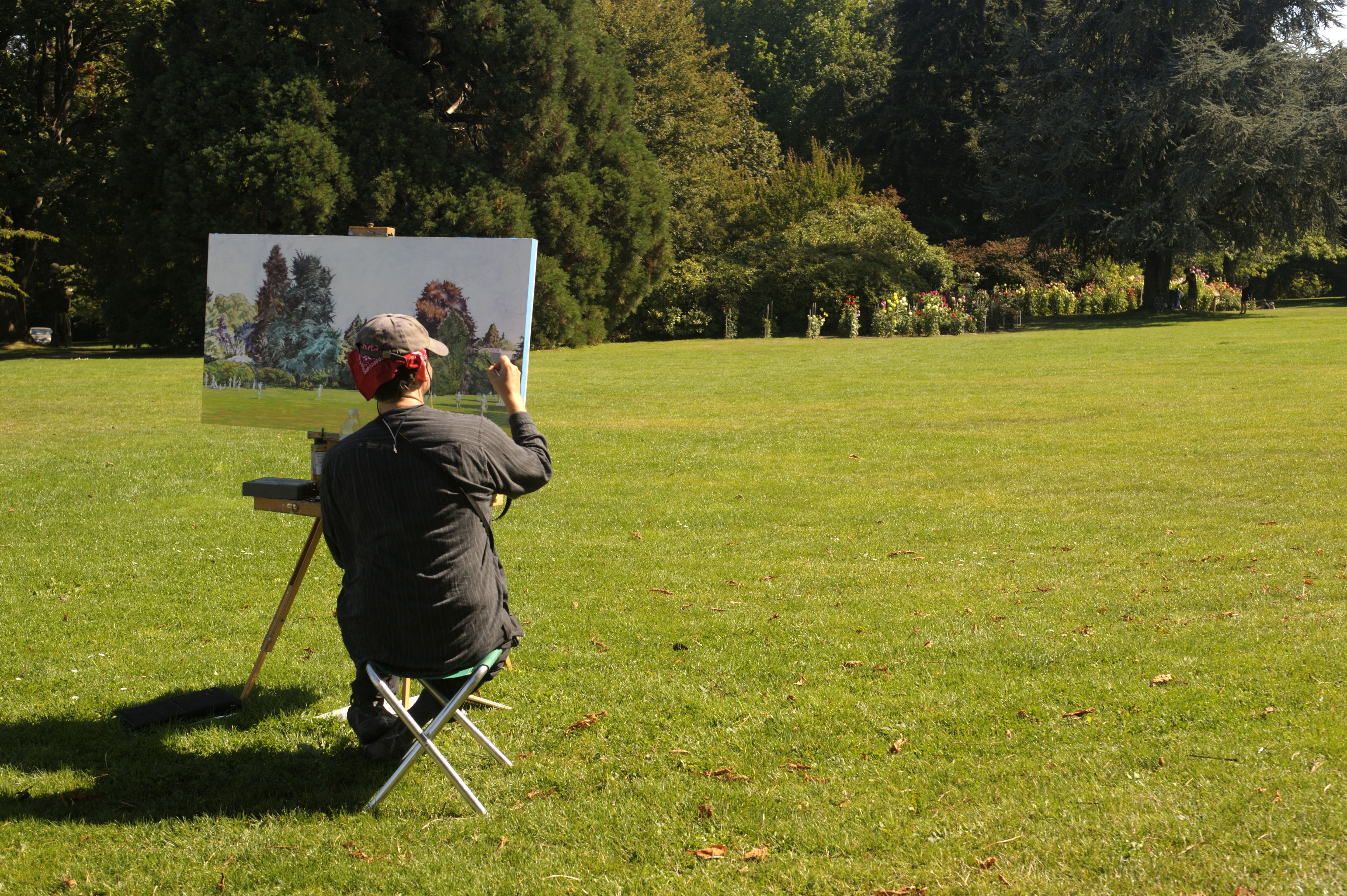 A photo of a the back of a person painting on an easel in a park.