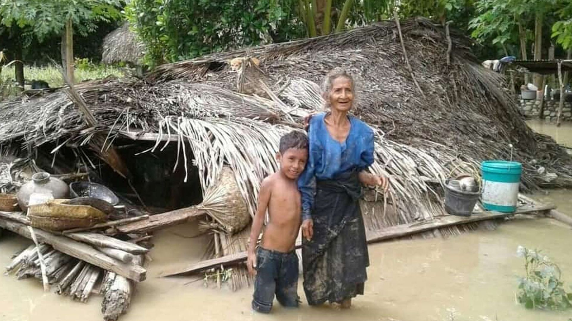 An elderly villager and her grandson stand in floodwaters in front of their damaged home in the village of Haitimuk in East Flores on April 4