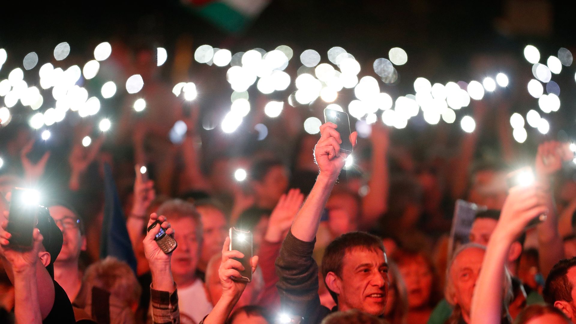 Protestors are lit up with red light and hold up phones lit up bright white.