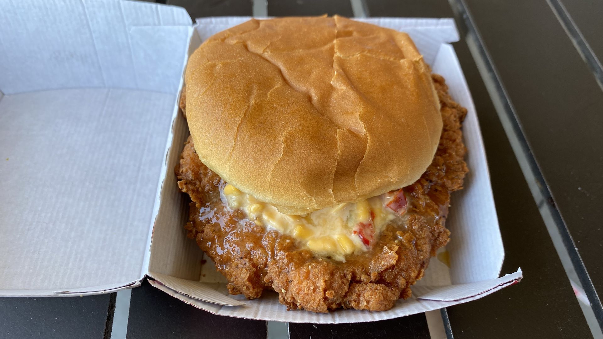 A piece of fried chicken with an orange and red sauce on it in a hamburger bun.