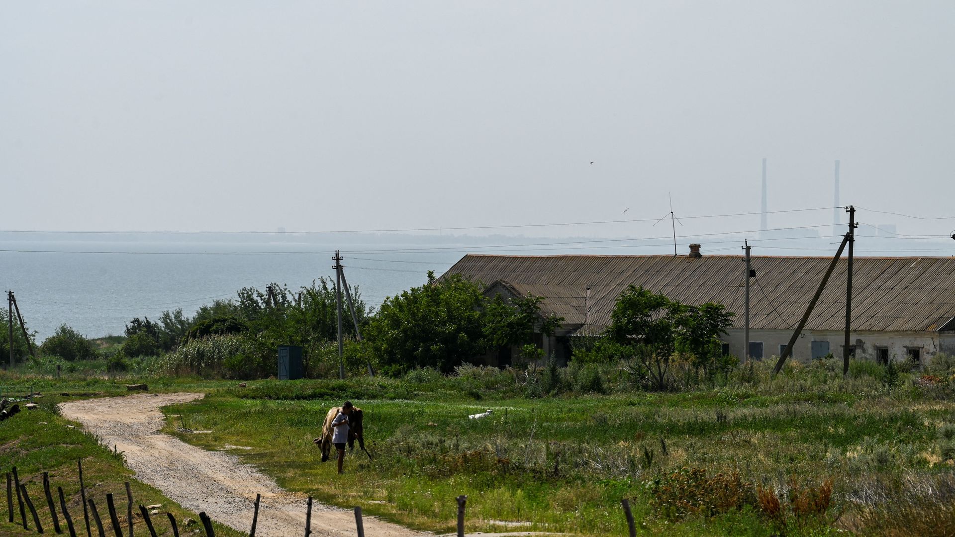 In this photograph taken on August 13, 2022 a local resident works in a garden in Vyschetarasivka as Zaporizhzhia nuclear power plant (Background-R) is seen across the Dnipro river.