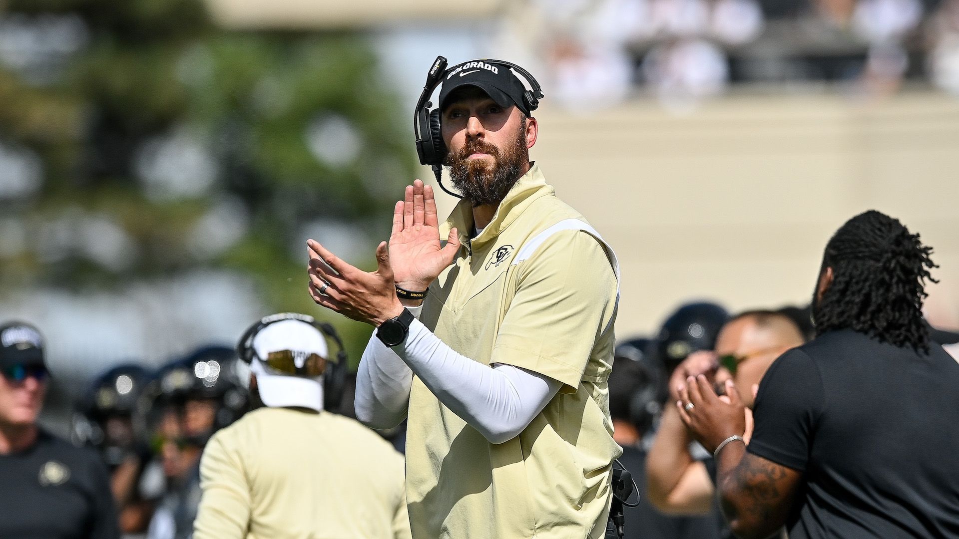A Colorado University football coach claps on the sidelines of a game. 