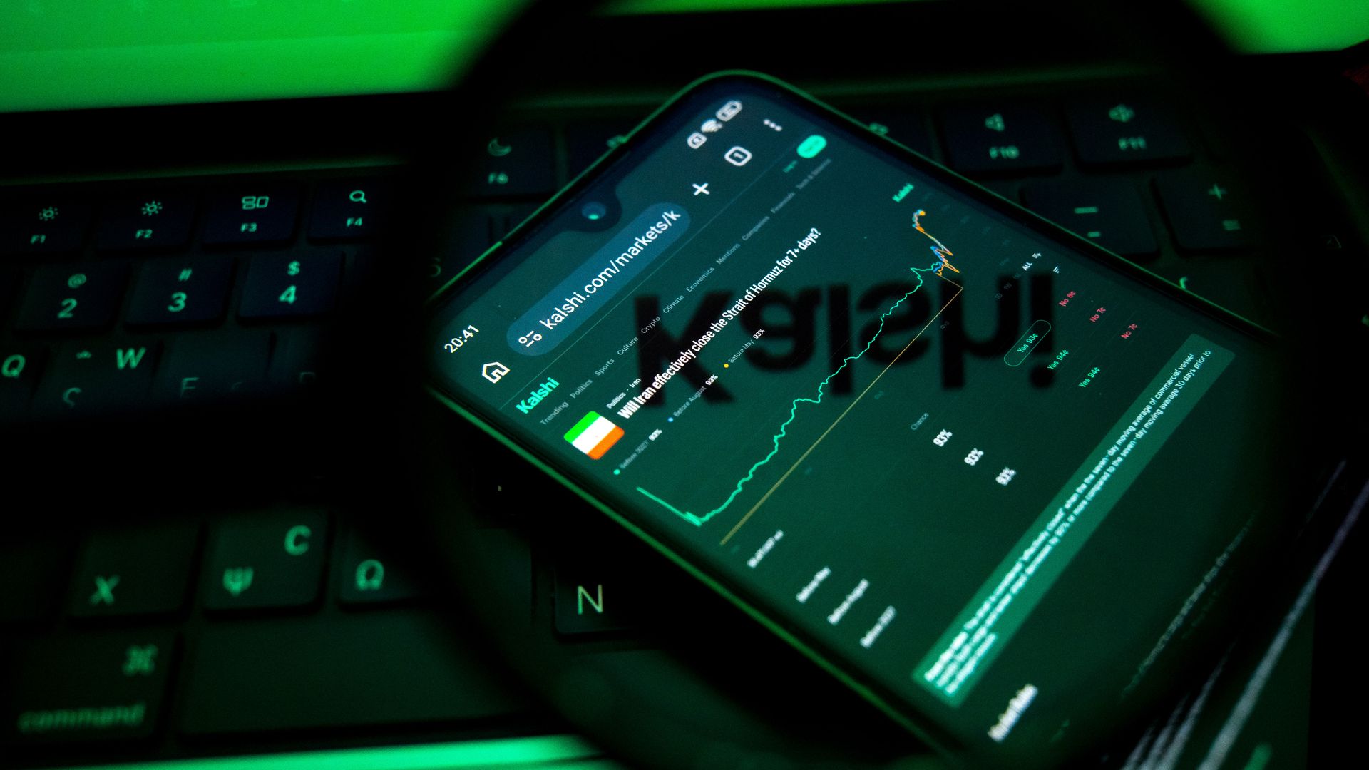 Close-up of a smartphone on a green-lit keyboard; the screen shows a dark chart with a bright green upward line and app icons, viewed through a magnifying glass.