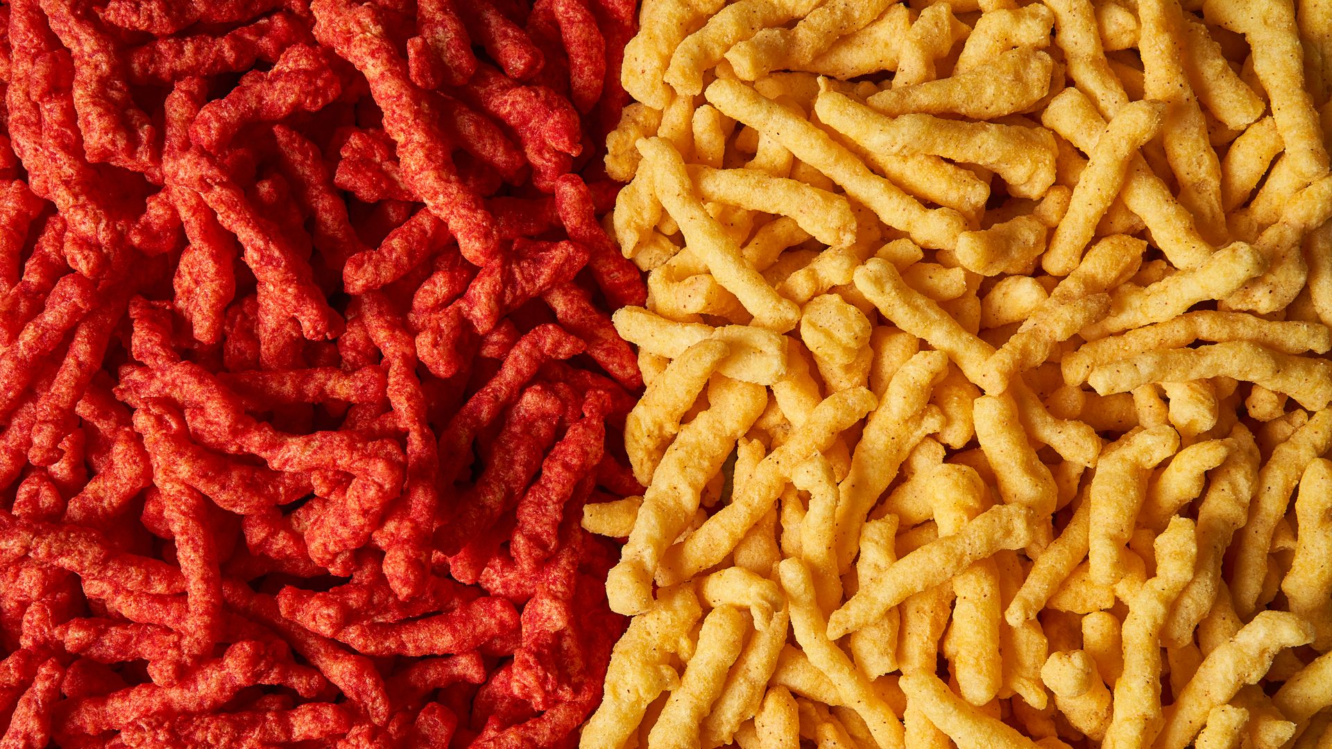 Close-up of red spicy snack sticks and yellow cheese-flavored snack sticks side by side, showing their crunchy texture and colors.