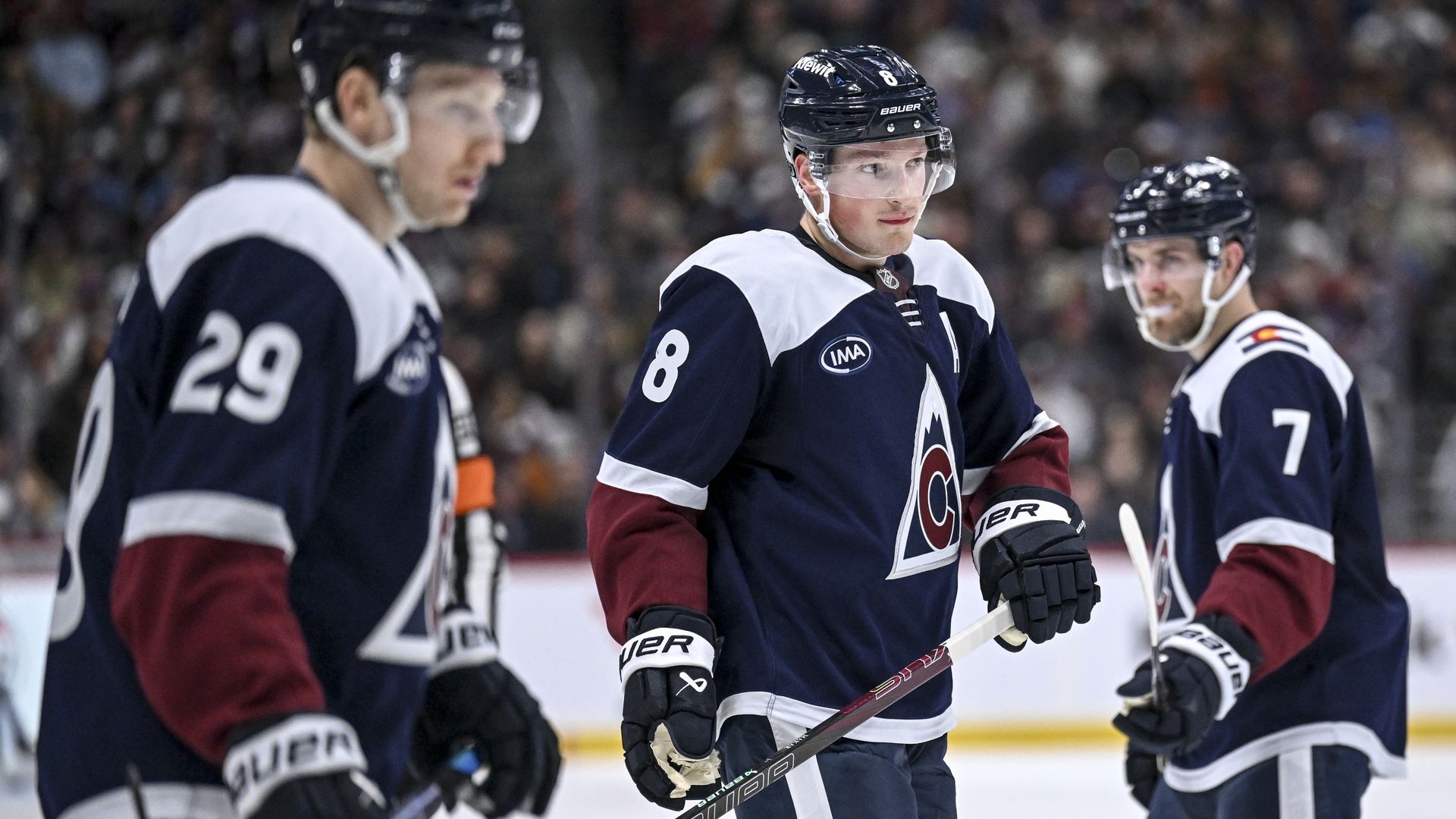 Three men in helmets and large jerseys wearing gloves, while one man holds an ice hockey stick.
