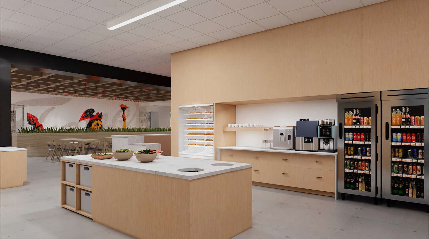 Bright, modern break room with light wood cabinetry, marble island with salad bowls, bread display, coffee station, beverage refrigerators, and a dining area with a mural in the back.