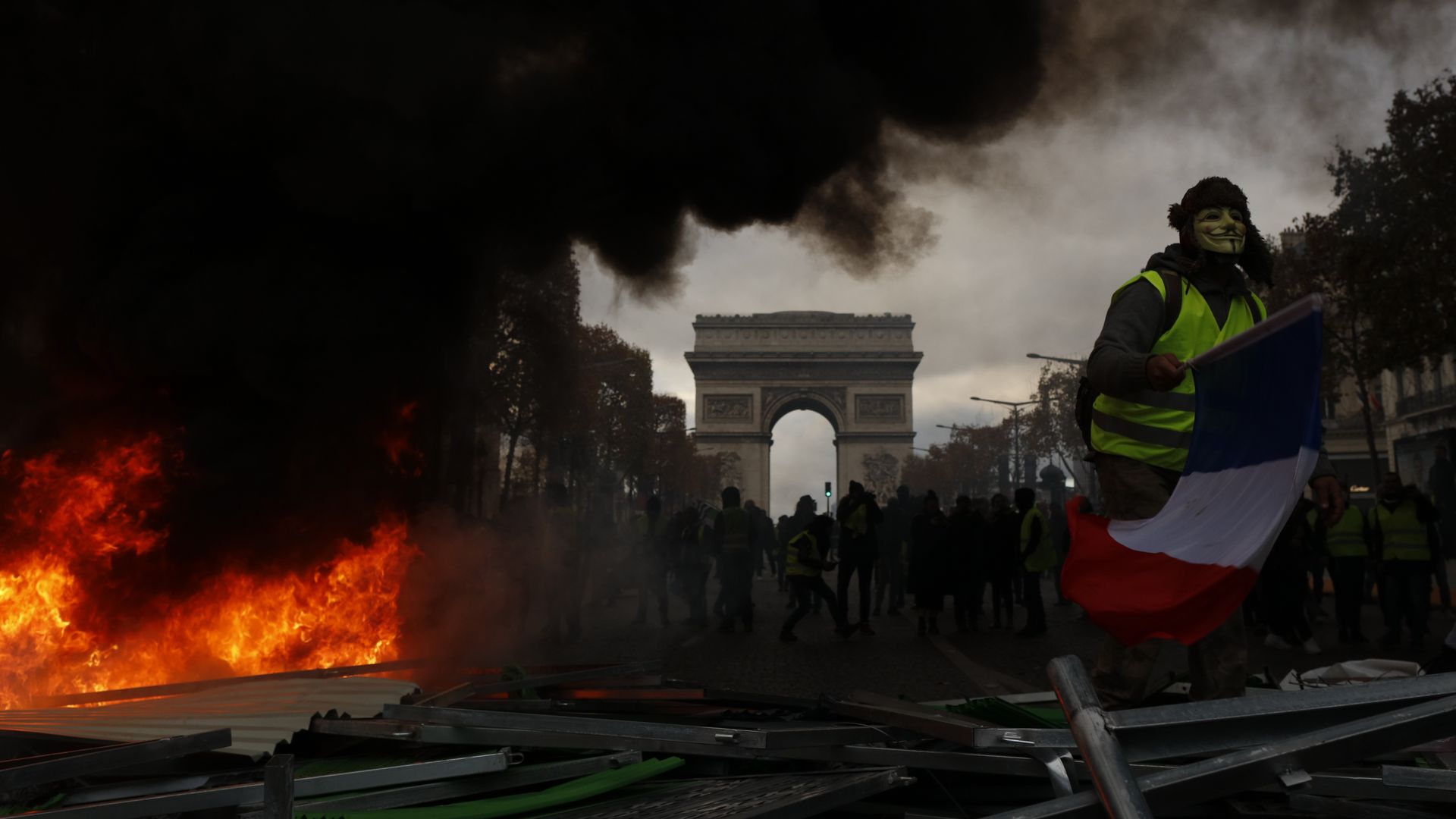 Yellow vests (Gilets jaunes) protestors shout slogans as material burns during a protest against rising oil prices and living costs near the Arc of Triomphe on the Champs Elysees in Paris
